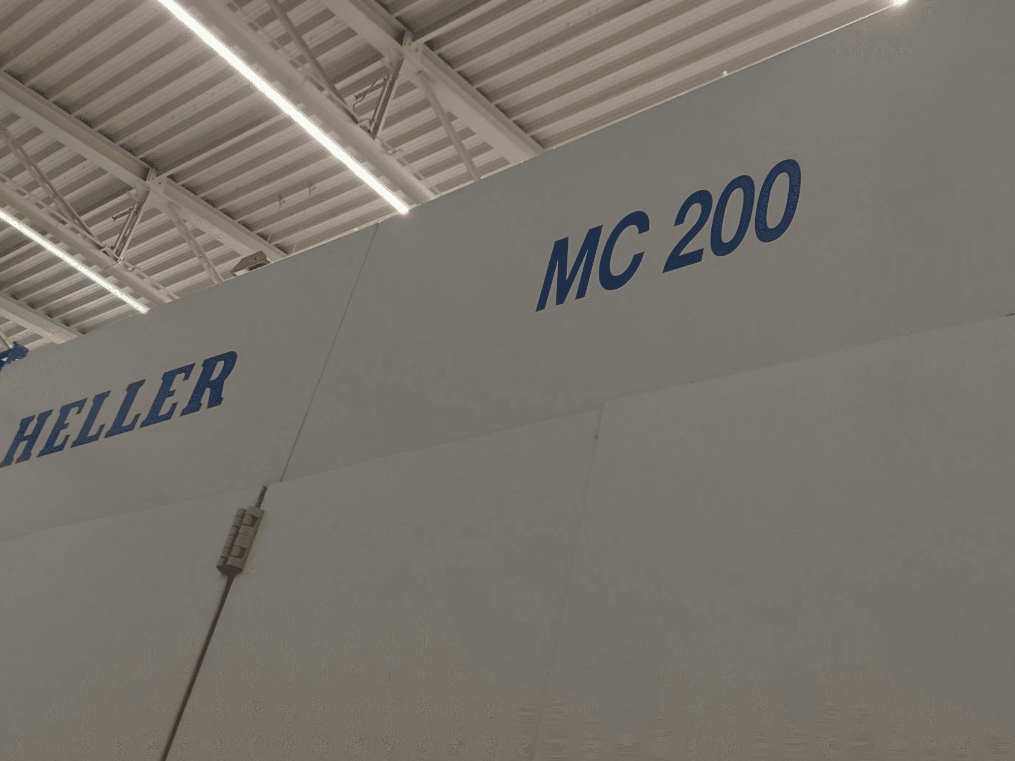Heller MC 200 horisontaalne töötluskeskus, kujutatud küljelt, rõhutatuna siniste tähtedega kaubamärgiga ja mudeliga valgel pinnal.