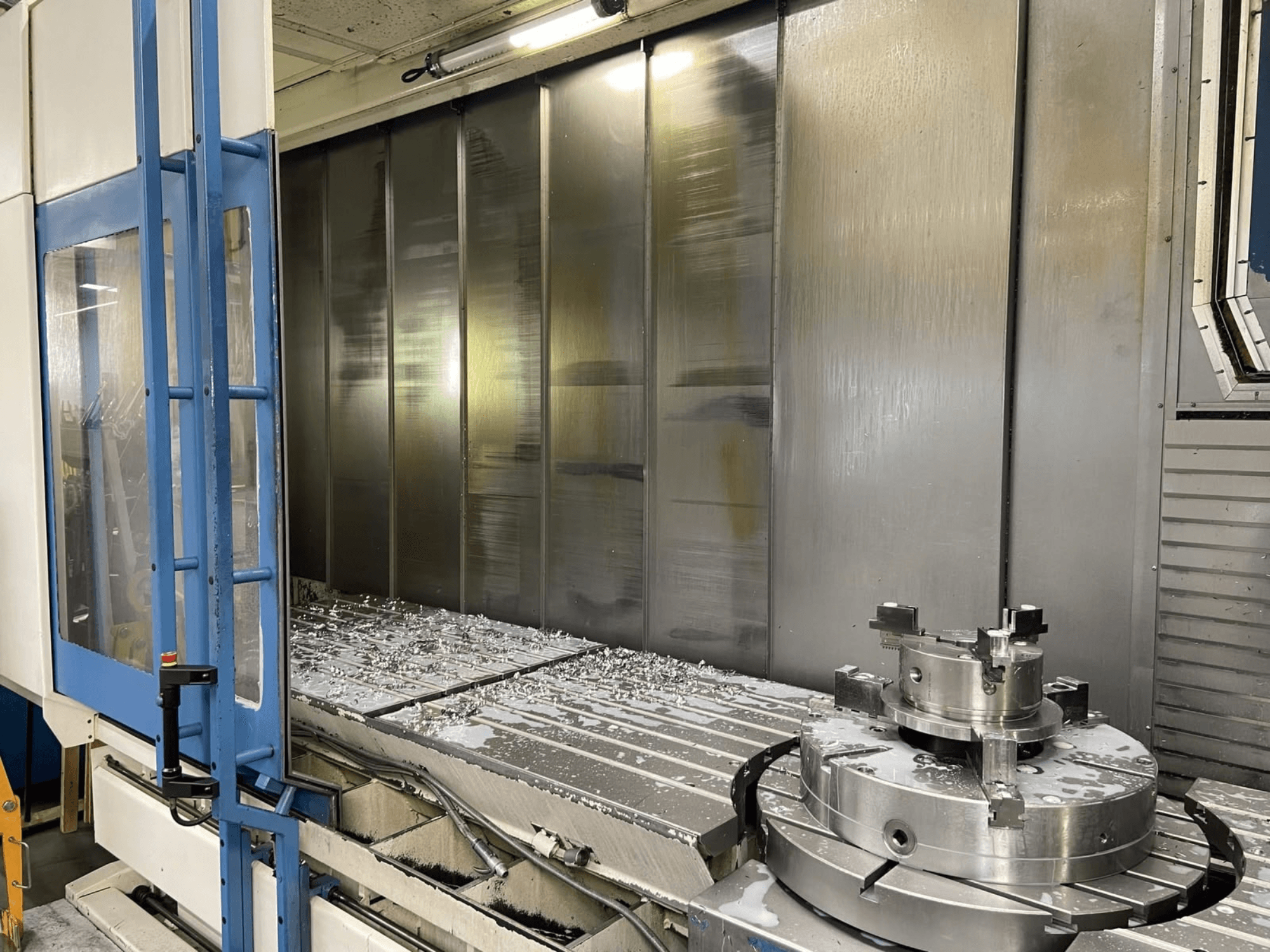 AXA VHC-3-3000-M/E vertikaalne töötlemiskeskus, vaade eest, millel on näha tööpinnal olevad freesitud metallilaastud ja lõikeriistad.