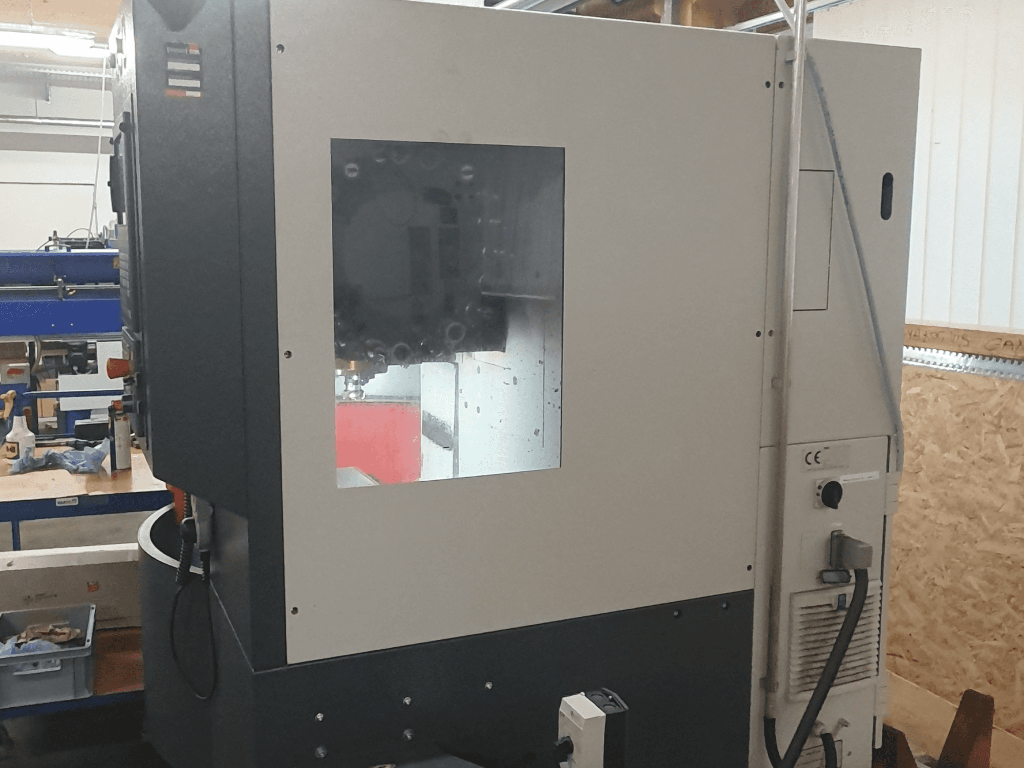 Külgvaade metallitöötlusmasinale, millel on nähtav juhtpaneel, suur vaateaken ja keerulised sisemised komponendid.