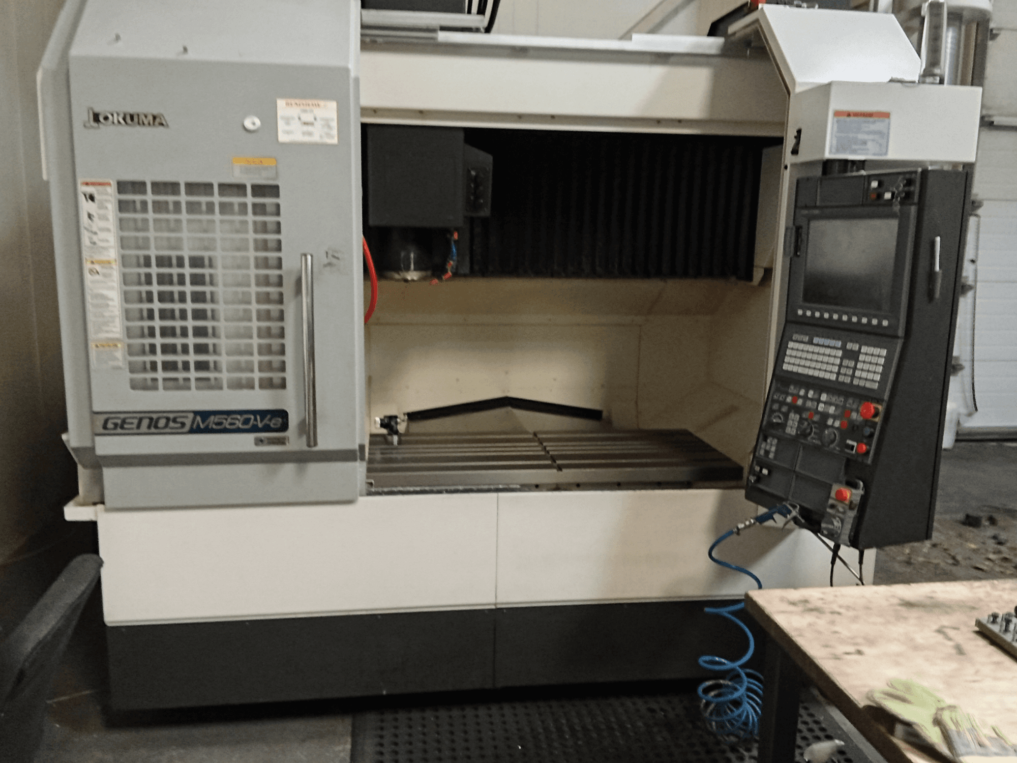 Okuma GENOS M560-V, vertikaaltöötluskeskuse esivaade juhtpaneeli, CNC-liidese ja nähtava lõikepinnaga.
