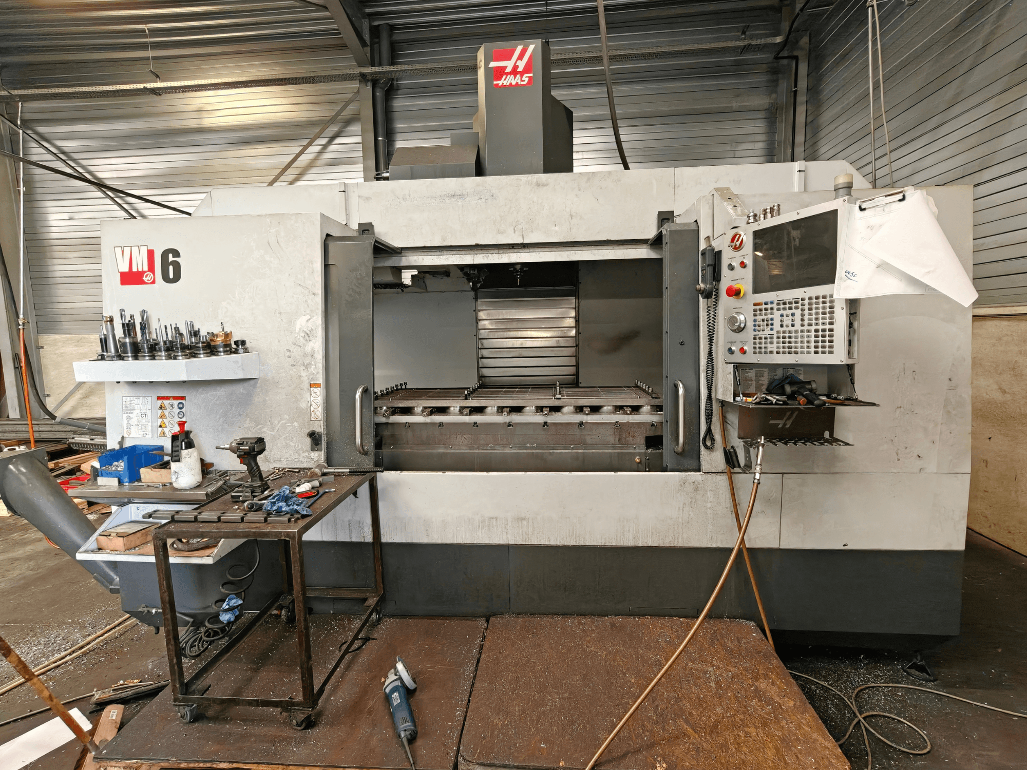 Haas VM-6 vertikaalne töötlemiskeskus, vaade eest, millel on näha tööriistade hoiuruum, juhtpaneel ja tööpinnal olevad töötlemisjäägid.