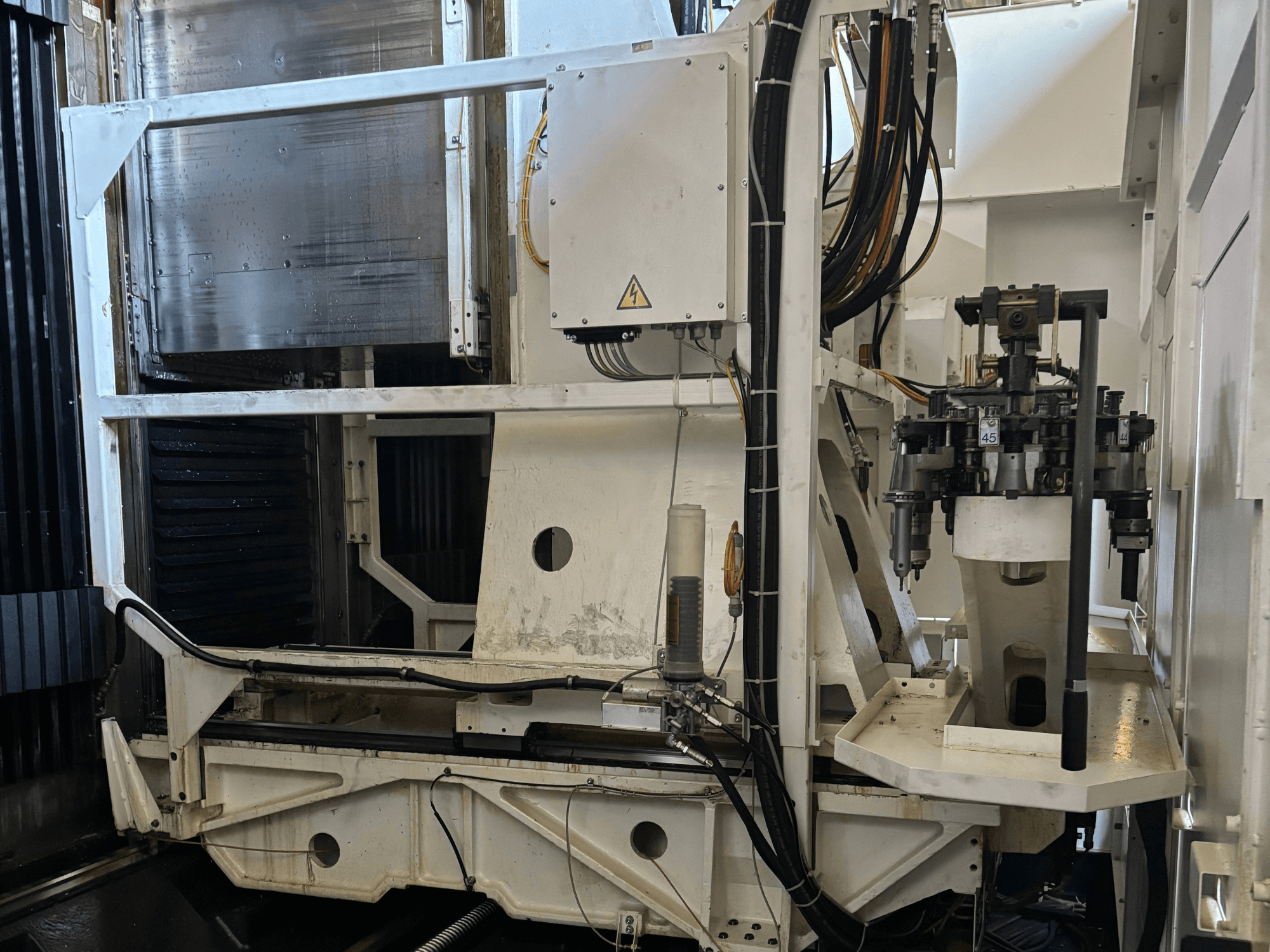 Tööstusmasina külgvaade, millel on näha valge CNC-freespingi koos nähtavate tööriistade, torude ja juhtpaneeliga.