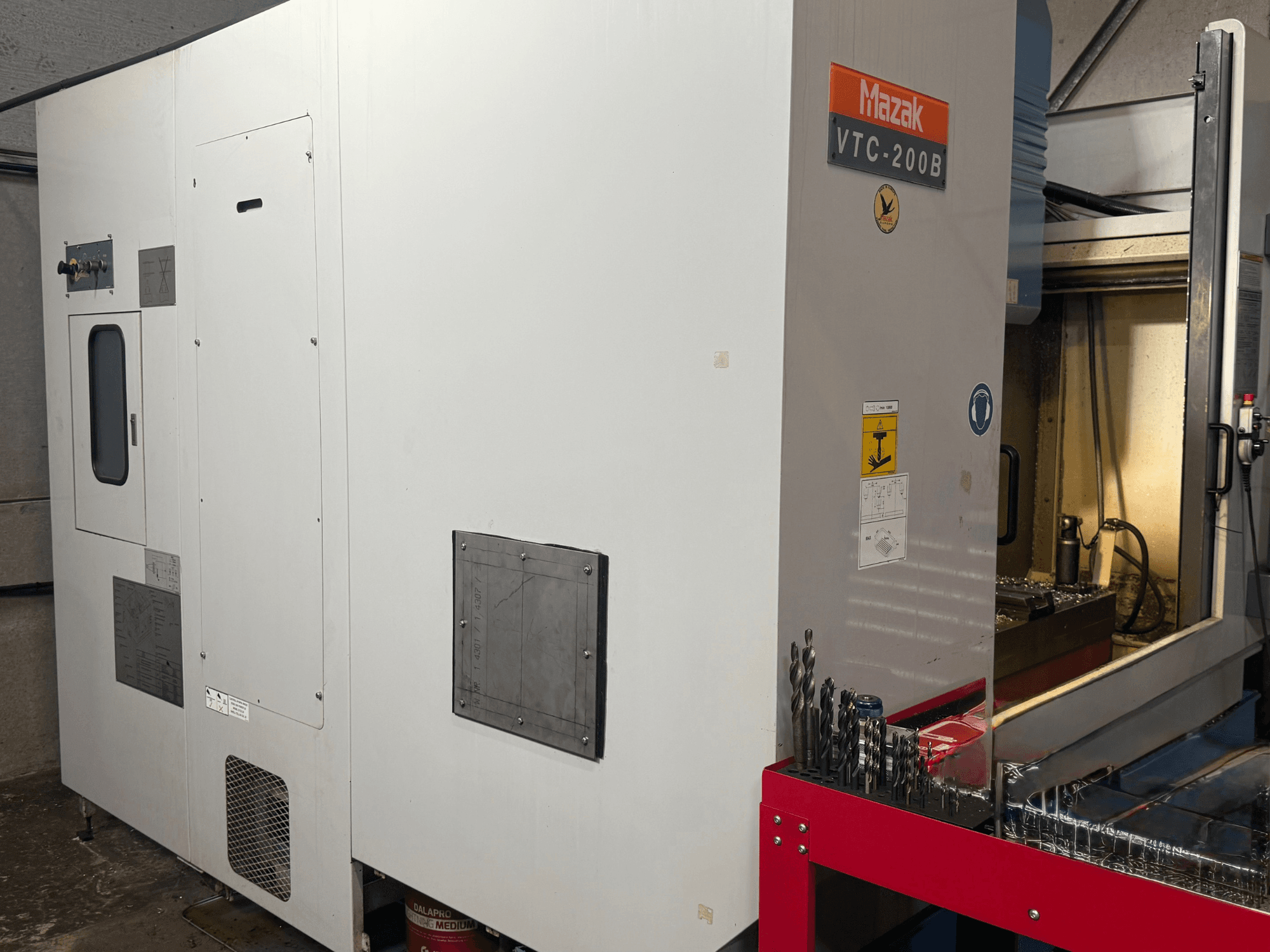 Mazak VTC-200B vertikaalne töötlemiskeskus külgvaates, millel on märgistatud juhtnupud ja punasel hoiustamisrestil asuvad puurid.