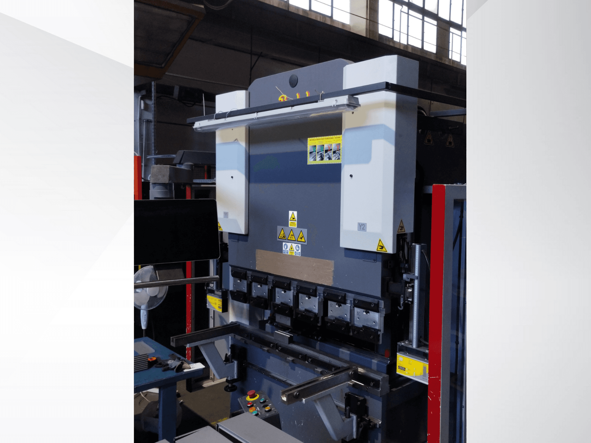 Presspidurmasin, esiplaanil. Omadused nähtavad juhtimisseadmed, ohutuskleebised ja mitu stantsihoidikut täpseks painutamiseks.