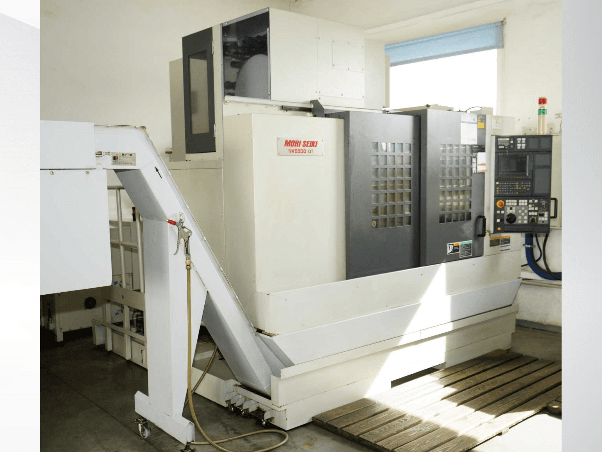 MORI SEIKI NV 5000 alpha1 vertikaalne töötlemiskeskus eestvaates, millel on näha juhtpaneel, ohutusseadmed ja laadimisala.