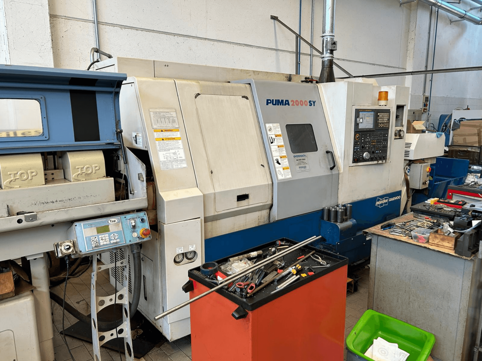 Töökojas asuv horisontaalne treipink DOOSAN PUMA 2000SY, külgvaade, millel on näha juhtpaneel ja selle lähedal asuvad tööriistad.