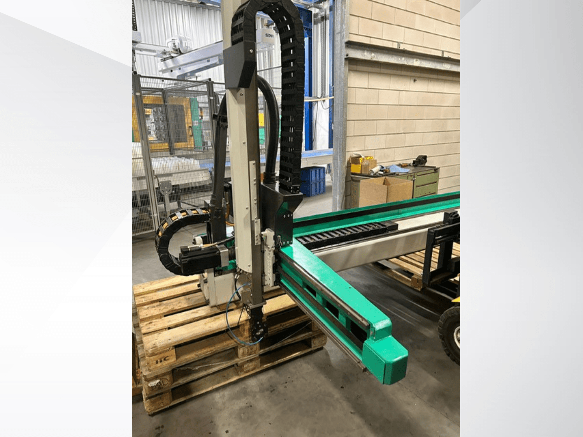 Arburg Multilift Select 15kg quer, külgvaade puitalustel olevast töödeldavast süsteemist, millel on näha robotkäsi ja juhtimiskomponendid.