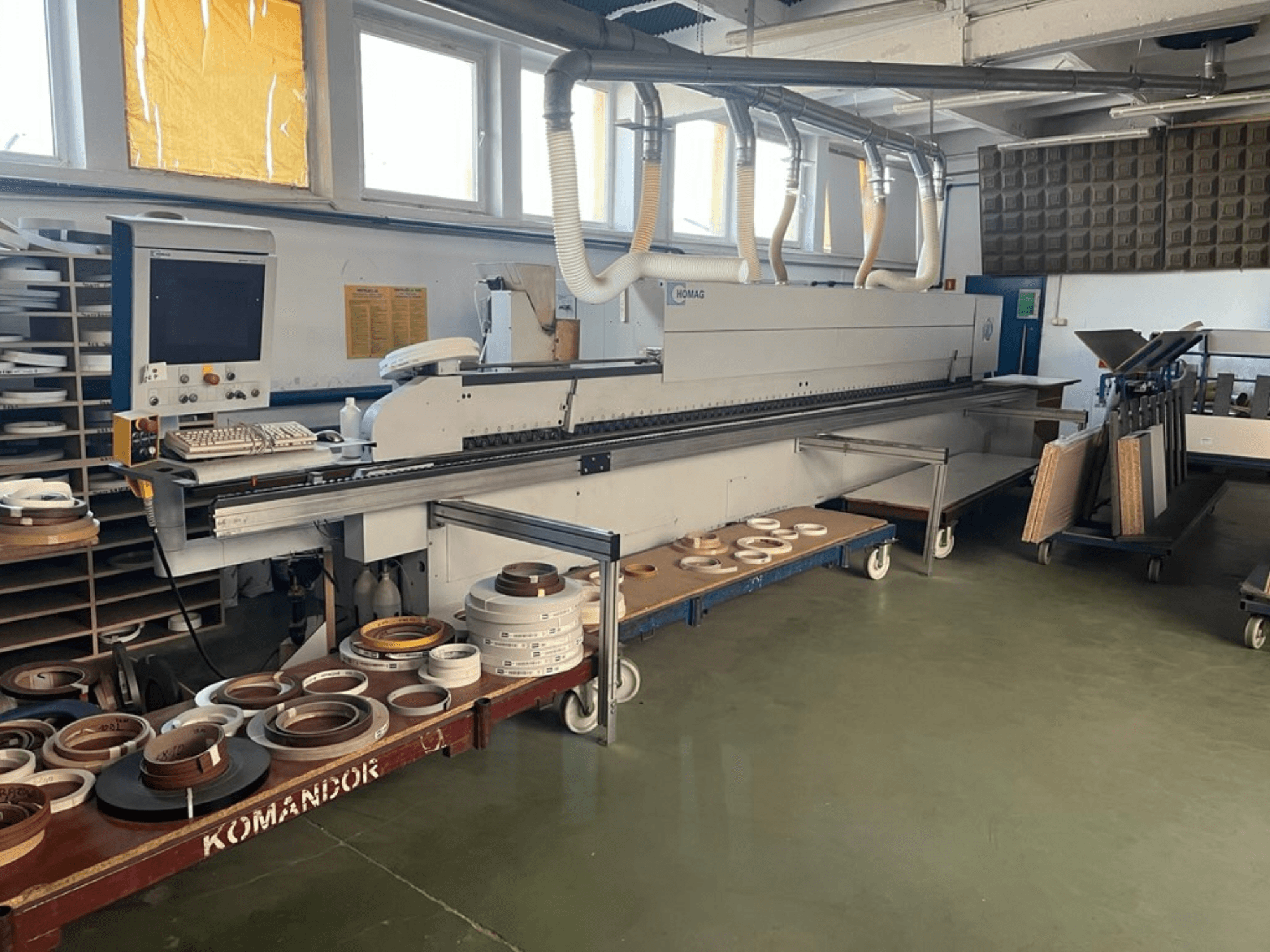 HOMAGi servapaigaldusmasin töökojas, millel on juhtimisseadmed ja erinevad servapaigaldusmaterjalid sinisel kärul. Külgvaade.