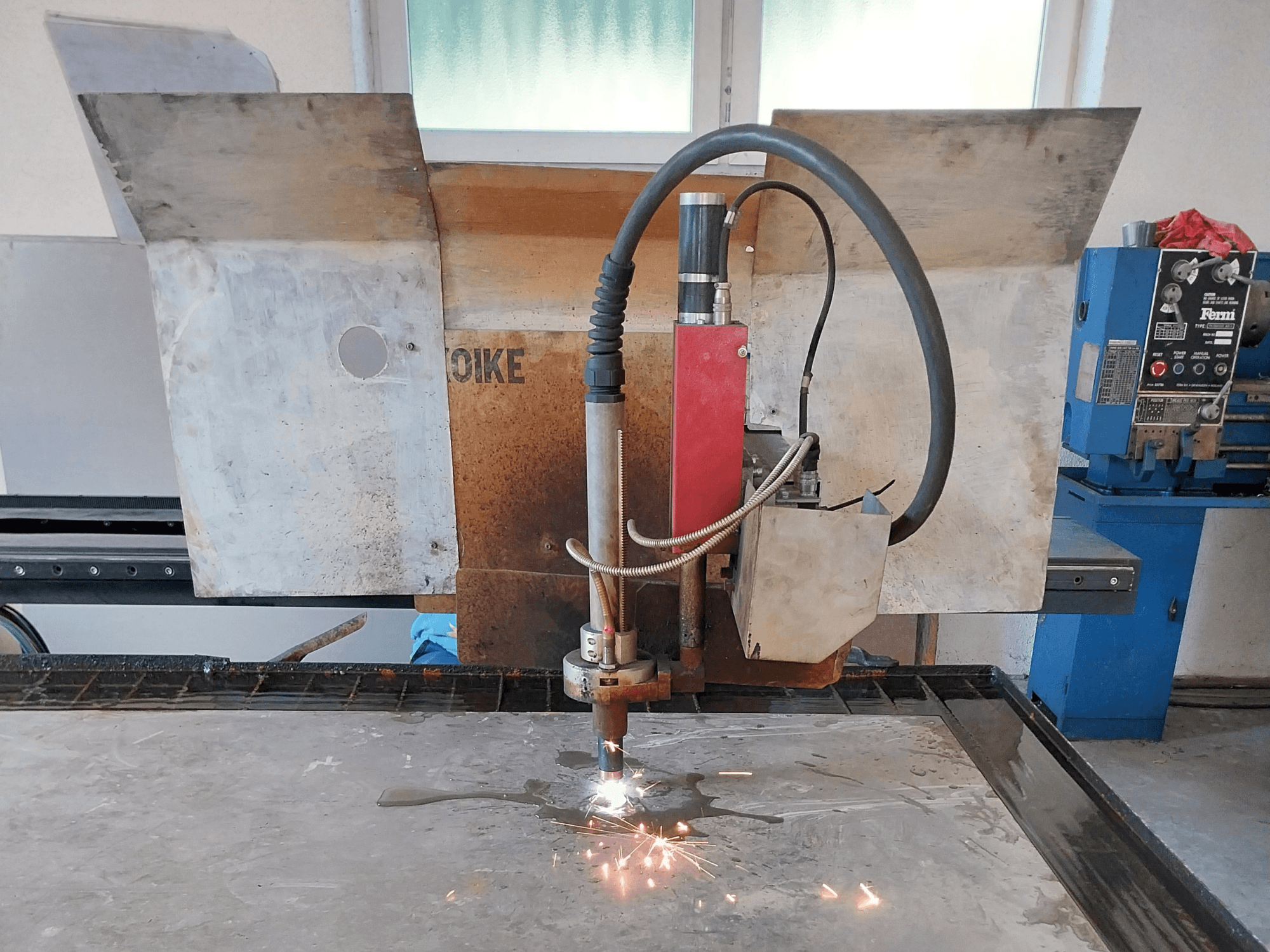 Esiküljepilt plasmalõikurist Oike, millel lendavad sädemed ja mis asub töölaual metallpinna kohal.