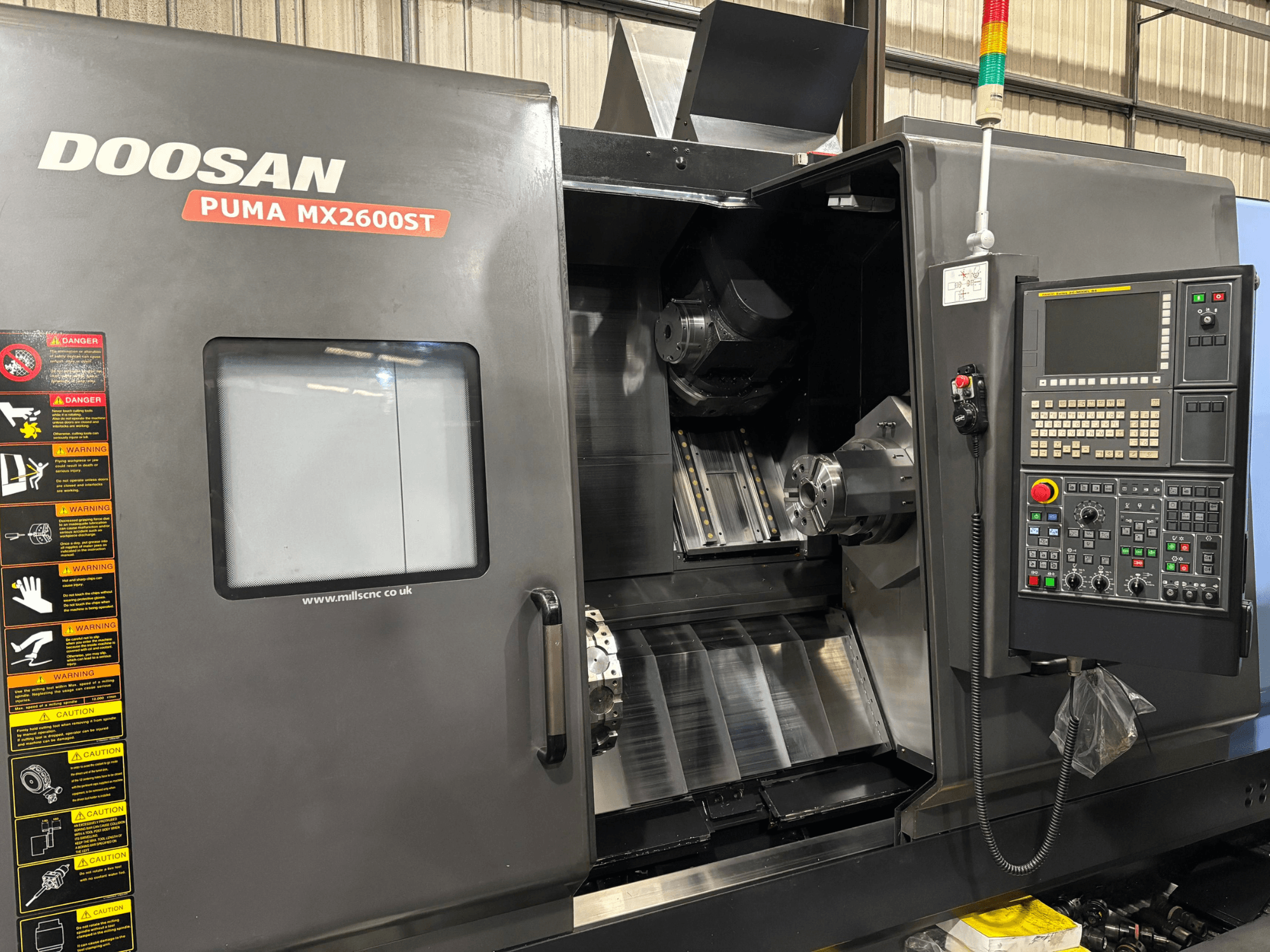 Doosan PUMA MX2600ST CNC-tööpink, esiplaan, kus on näidatud juhtpaneel, spindel ja töötlemisala koos nähtavate ohutushoiatustega.