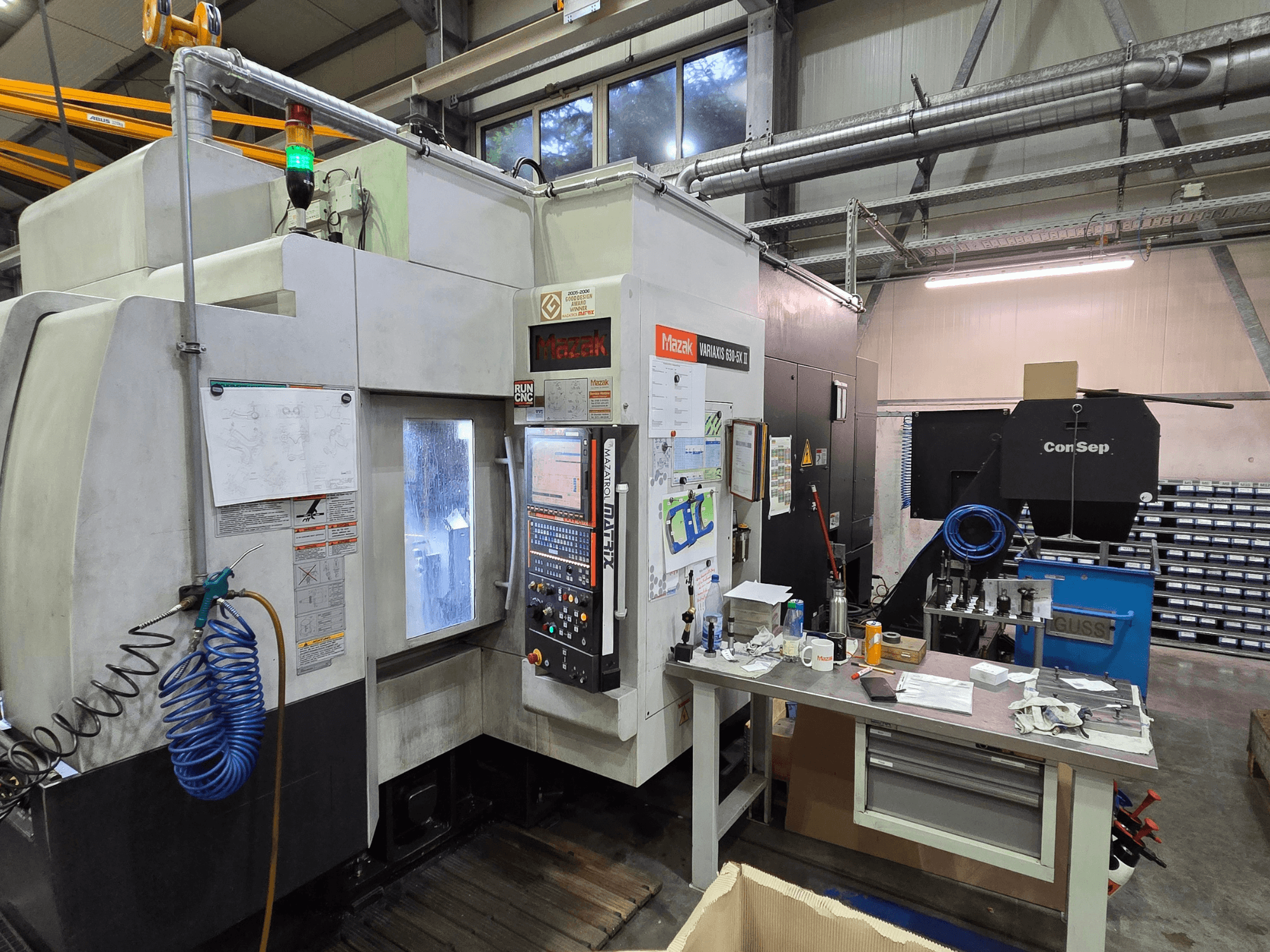 Mazak Variaxis 630-5X CNC-tööpink töökojas, esivaade juhtpaneeli, vooliku ja tarvikutega küljelauas.