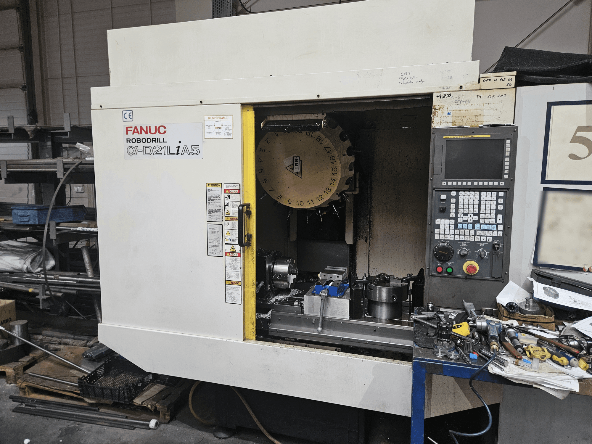 FANUC Robodrill α-D21LiA5, esiplaanil on tööriistahoidja ja juhtpaneel, mida ümbritsevad tööriistad ja seadmed töökojas.