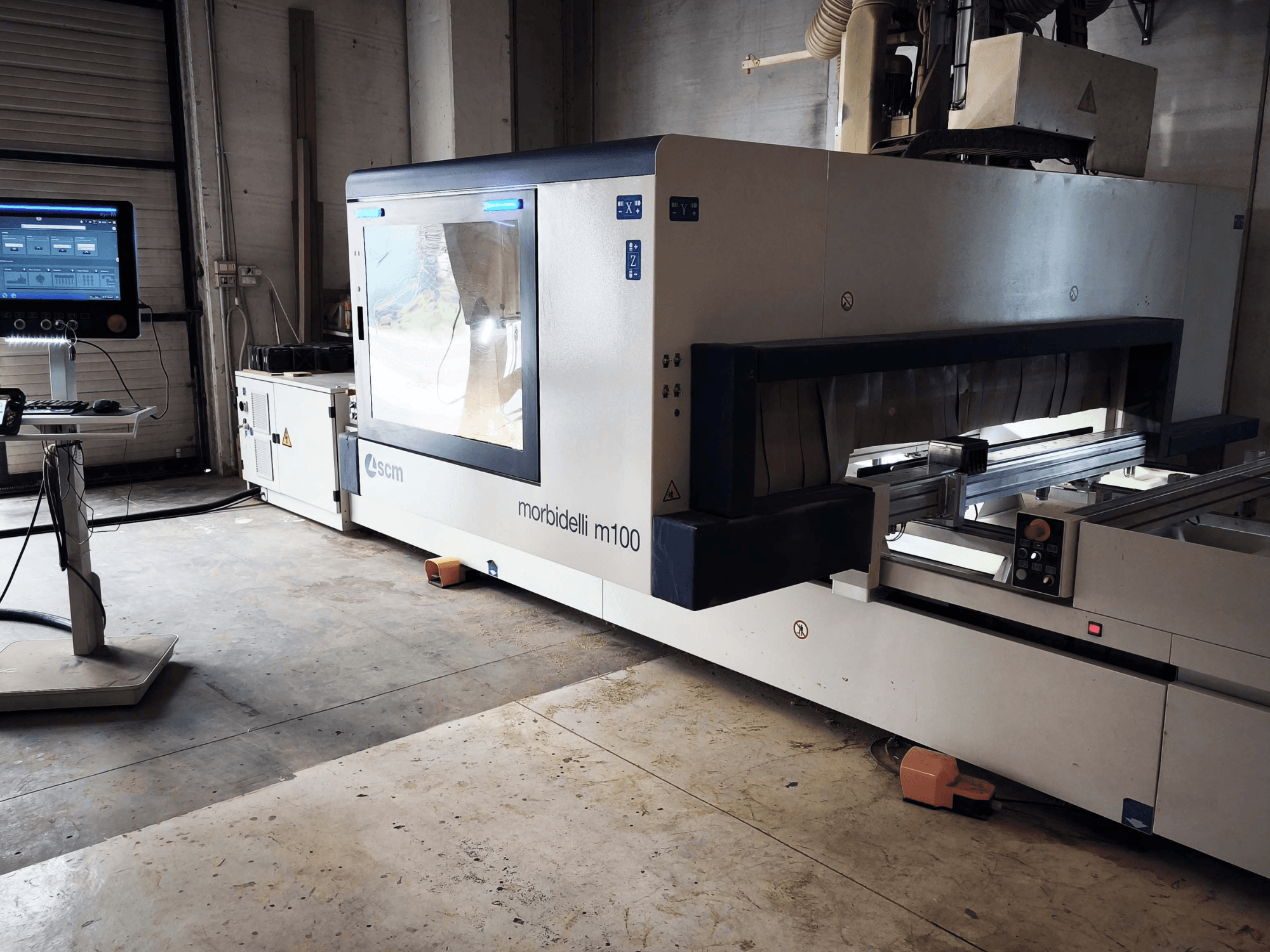 SCM Morbidelli M 100 CNC-puidutöötluskeskus külgvaates, millel on näha juhtpaneel, töötsoon ja ohutusseadmed.