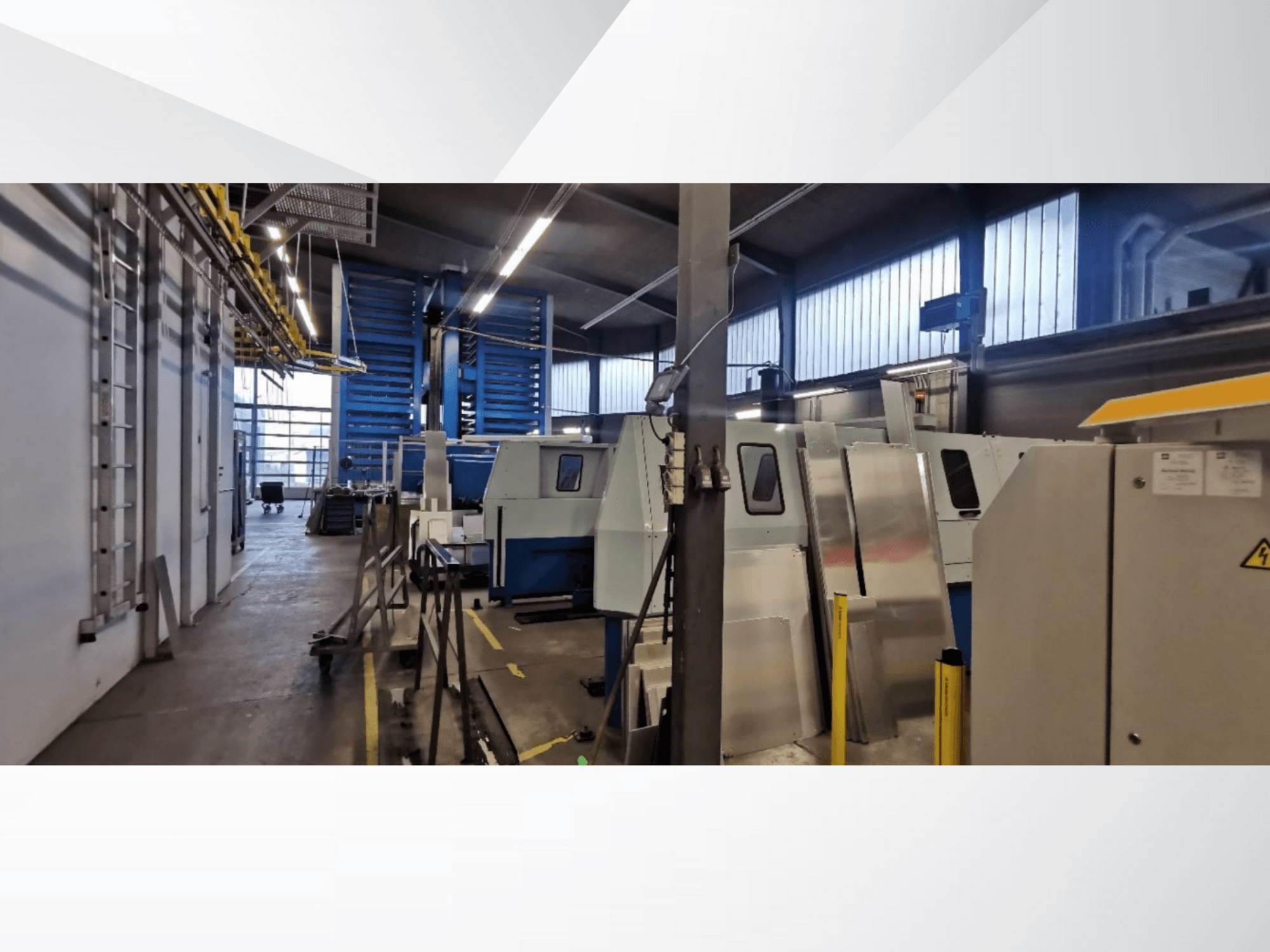 Tööstuslik töökoja stseen, millel on mitu masinat ja seadet külgvaates, metallist pinnad ja nähtavad ohutusseadmed.