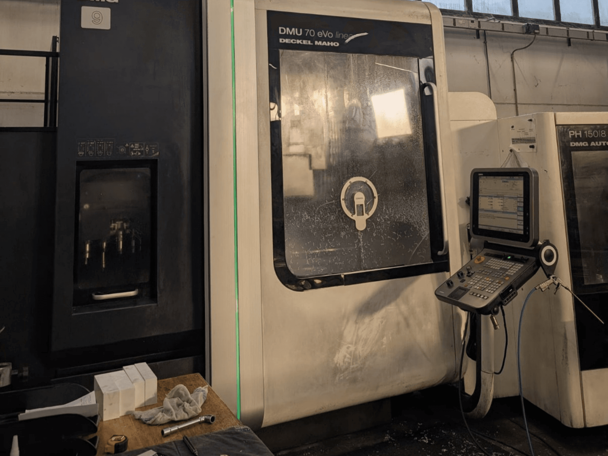 DMG DECKEL MAHO DMU 70 EVO Lineaarne vertikaalne töötluskeskus, esiplaan, kus on näha juhtpaneel, tööriistad ja tööruum.