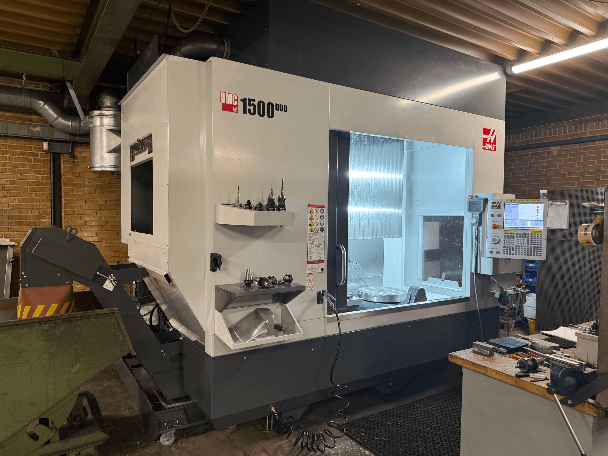 Haas UMC 1500DUO CNC-pink, esivaade, millel on suur aken, juhtpaneel ja riiulil olevad tööriistahoidjad.
