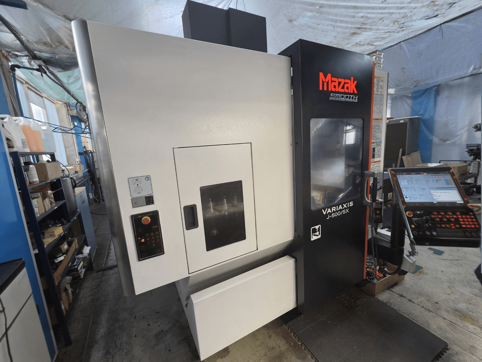 Mazak VARIAXIS J-500/5X vertikaalne töötlemiskeskus eestvaates, millel on juhtpaneel ja suur töötlemisala aknaava.