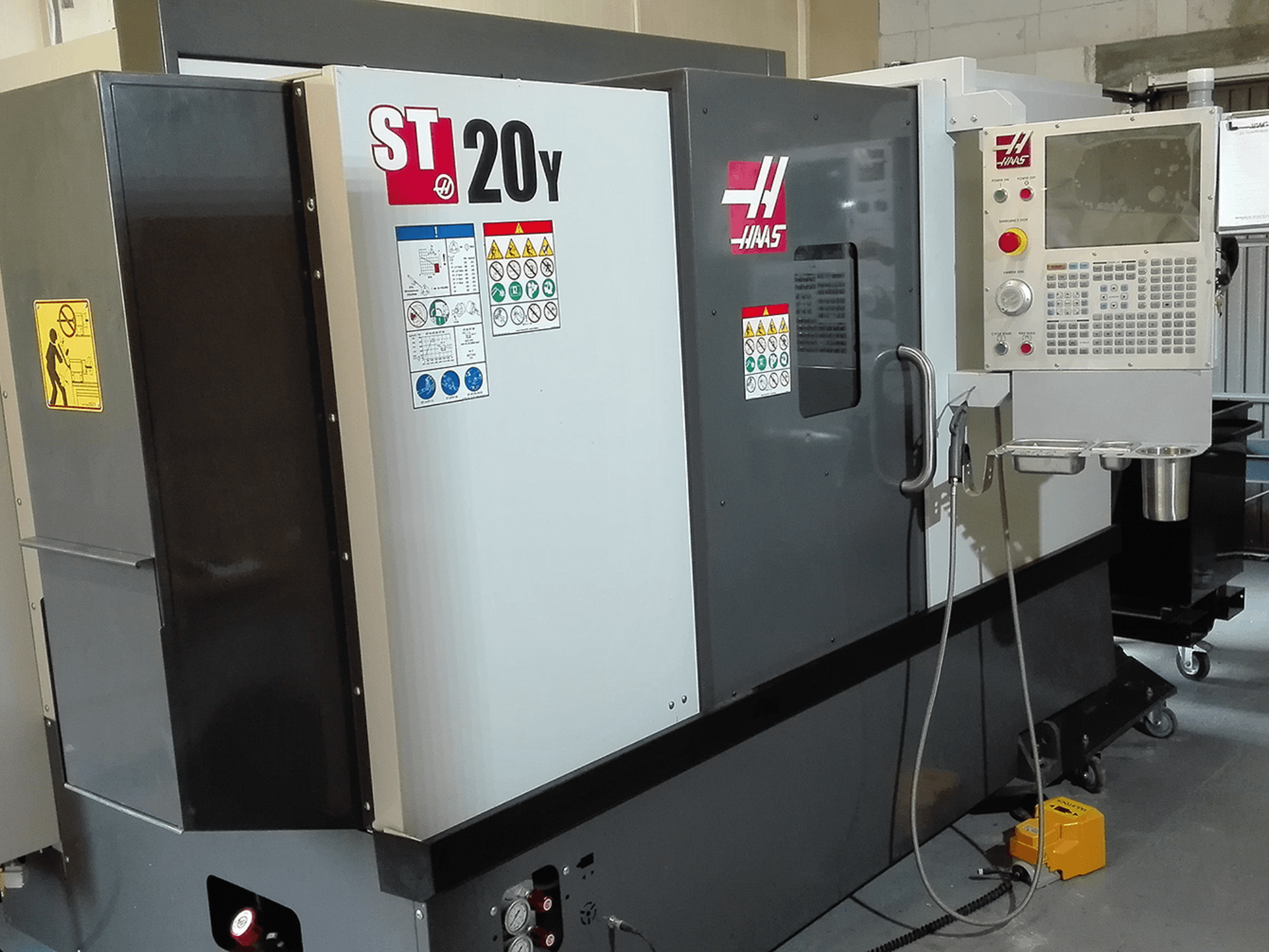 Haas ST20Y CNC-teeninduspingi esiplaan, millel on tööpaneel, ohutussildid ja jahutusvedeliku süsteem.