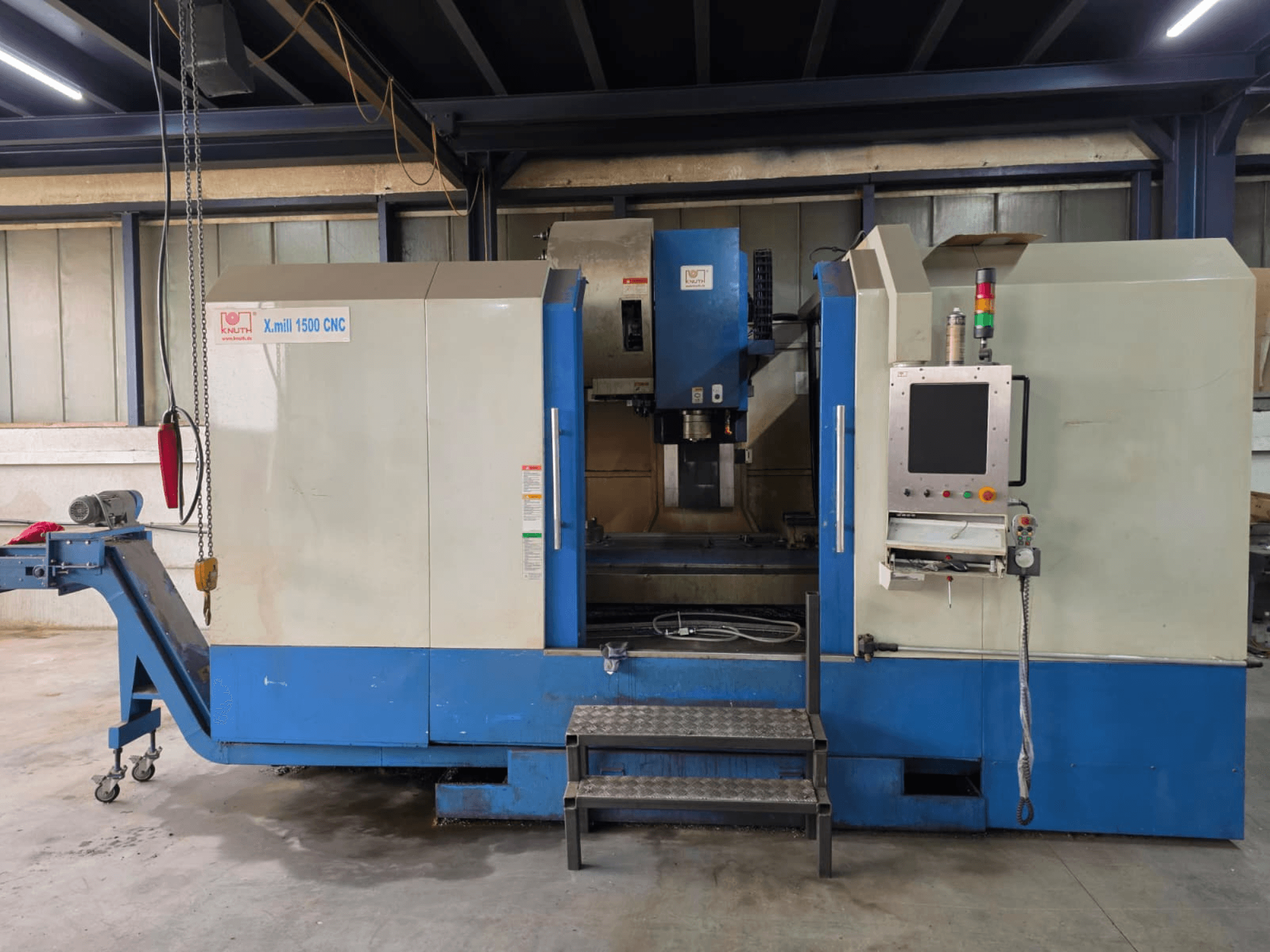 CNC-vertikaalne töötlemiskeskus KNUTH X-MILL 1500, külgvaade, millel on näha juhtpaneel, astmed ja väljundkonveier.