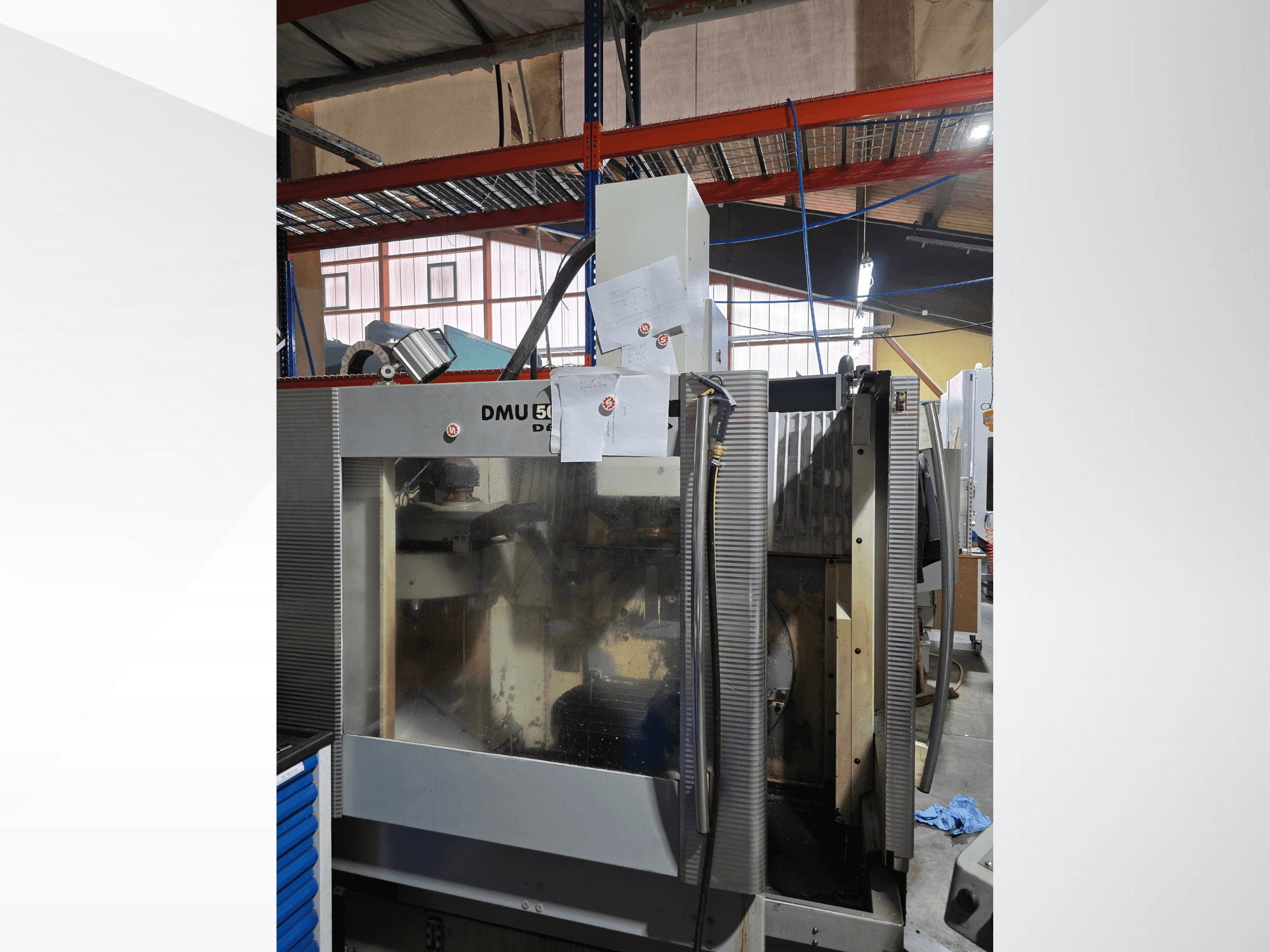 DMU 50 3-teljeline CNC-töötluskeskus töökojas, näidatud esiplaanilt, millel on näha töötavaid komponente ja lisatud dokumente.