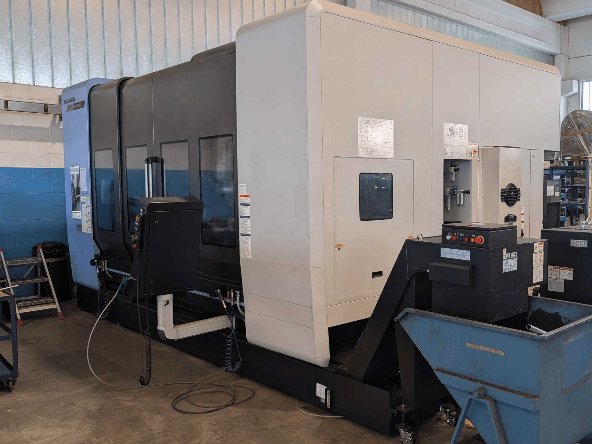 DOOSAN VCF850LSR-II vertikaalne töötlemiskeskus külgvaates, millel on näha juhtpaneel, jahutussüsteem ja tugev konstruktsioon.