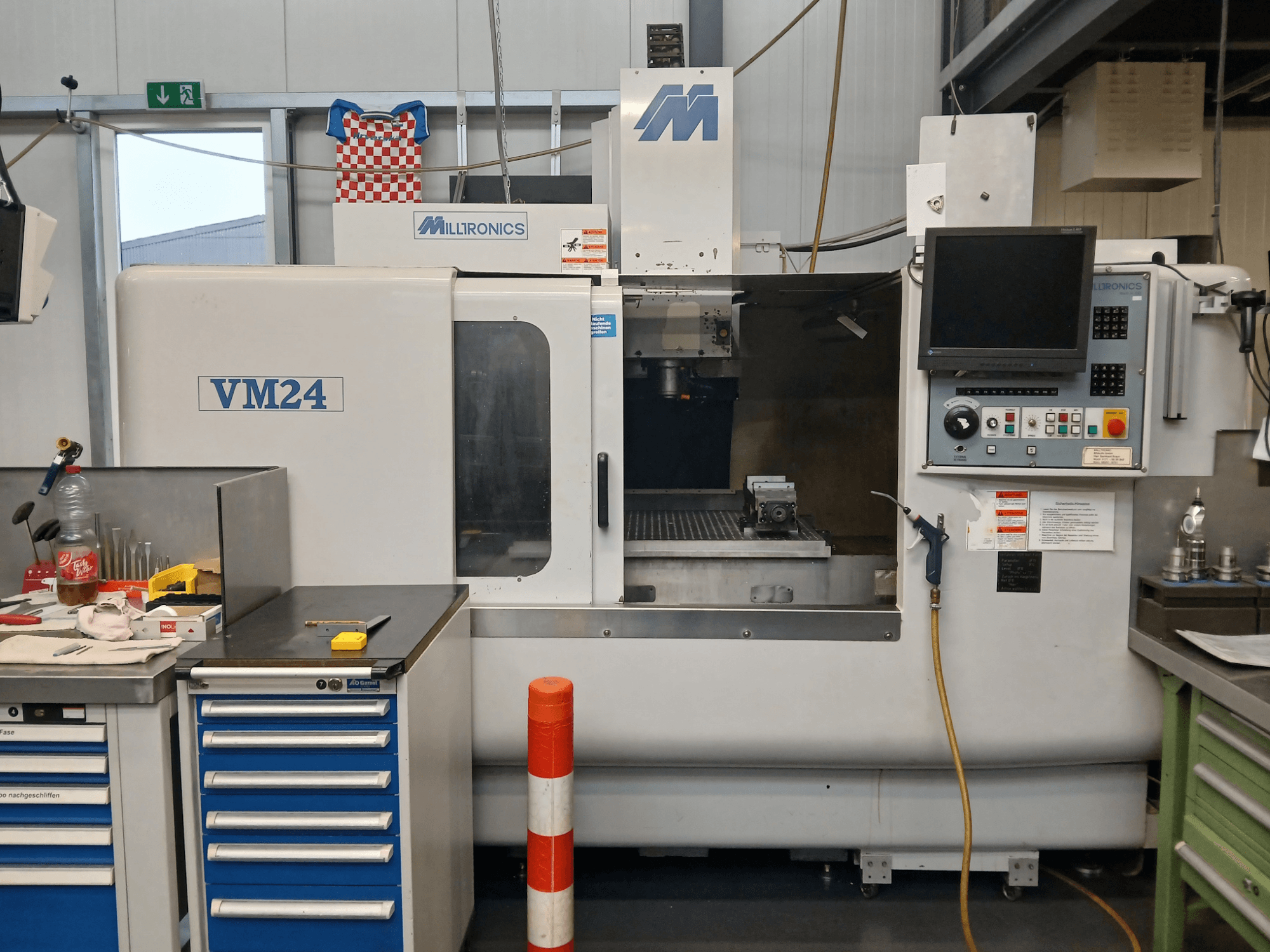 Milltronics VM24 CNC-freesping, mis on näidatud esiplaanilt, kus on juhtpaneel, tööriistade hoidla ja tööpiirkonna seadistus.