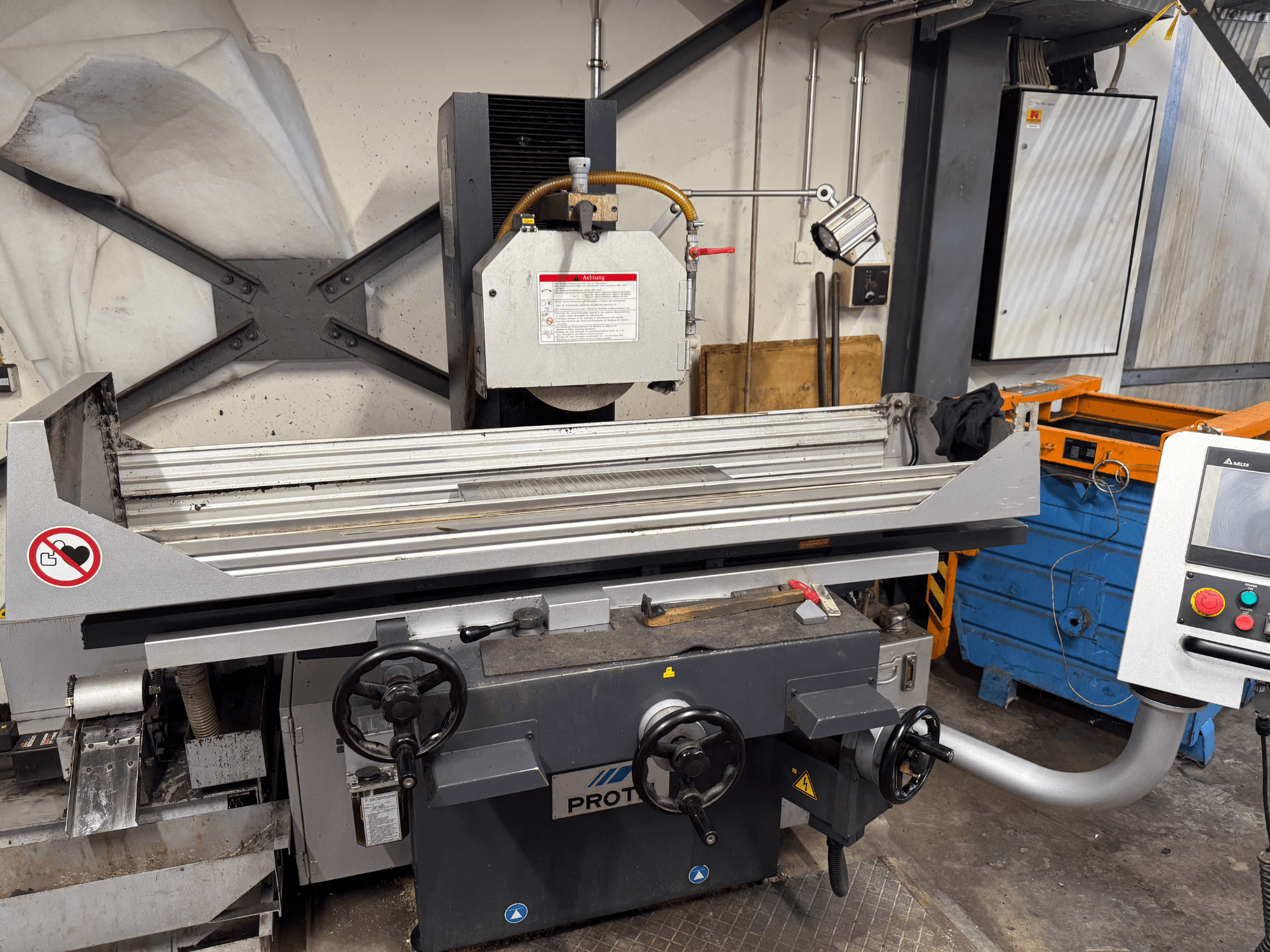 PROTECi masin, esiplaanil, millel on kujutatud pinnahöövlimasin koos käsitsi juhtseadmete, ohutushoiatuste ja jahutussüsteemiga.