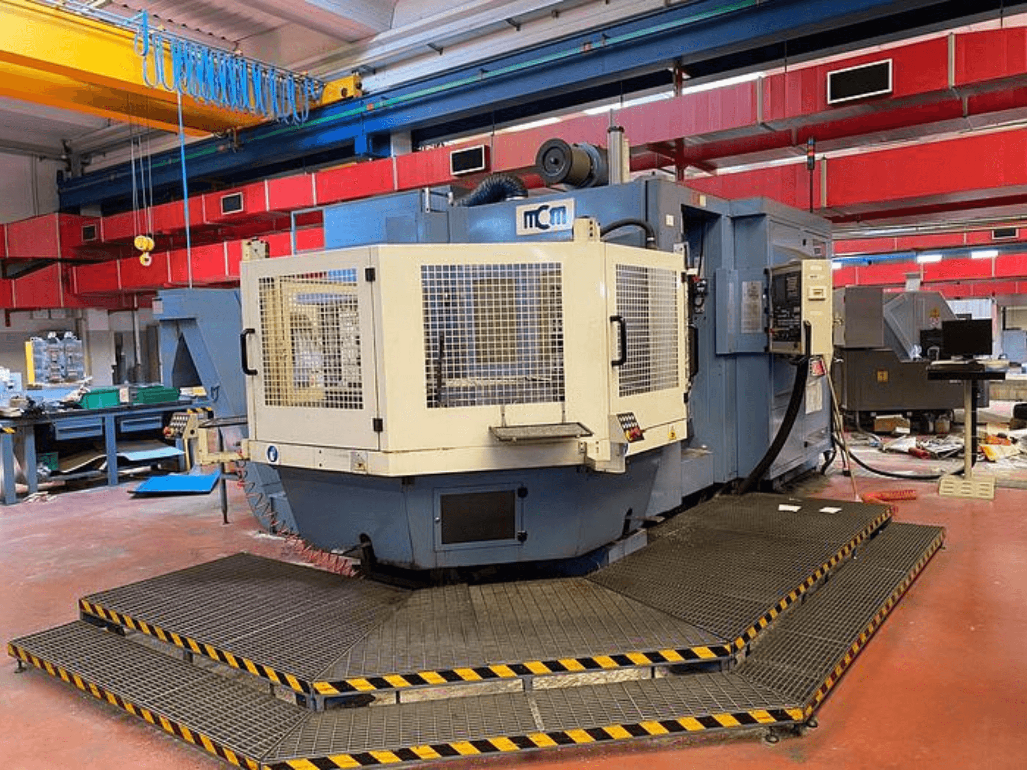 MCM CNC masin tehases, esivaade kaitsekorviga, mustad ja kollased kaitseservad, ümbritsetud tööstusseadmetega.