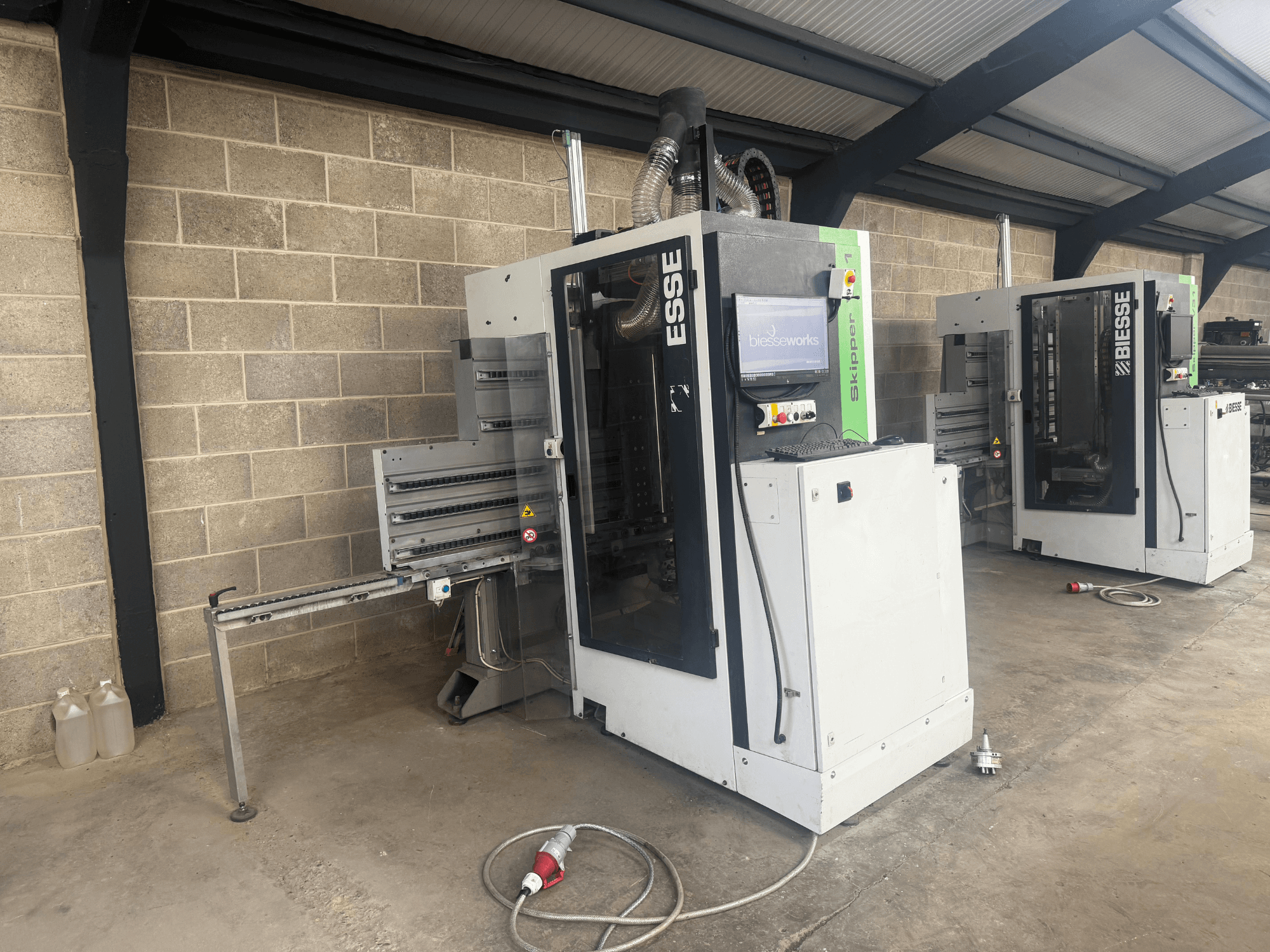 BIESSE Skipper v31 puidupuurmasin külgvaates, millel on juhtpaneel ja kõrvalolevad masinad, töökojas.