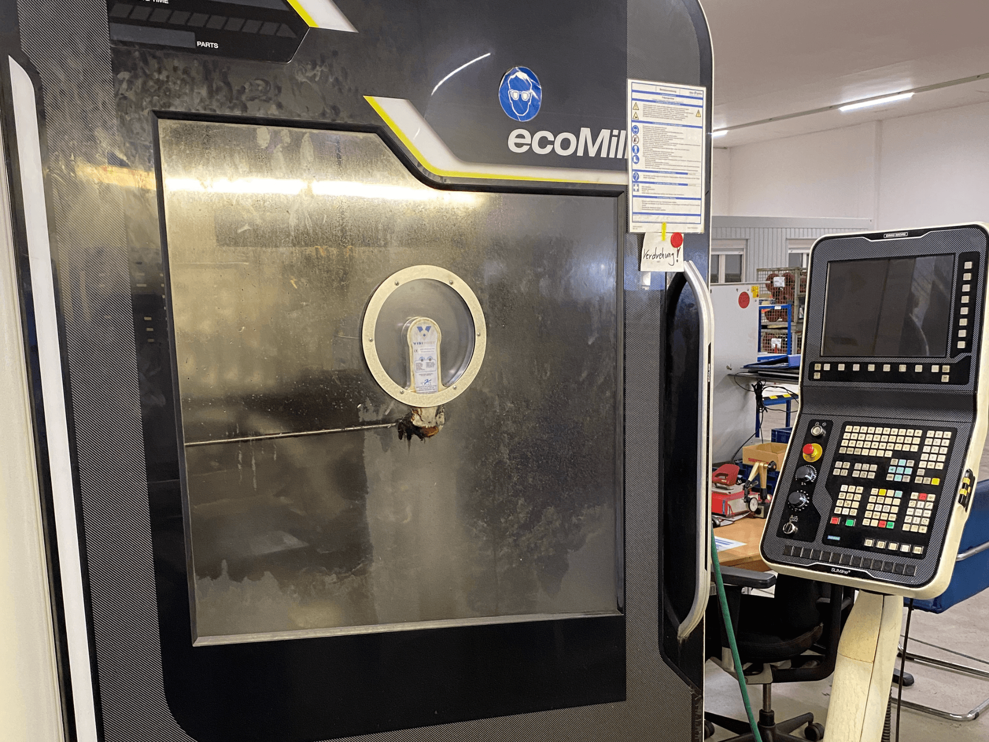 DMG MU 70 ECO freesmasin eestvaates, millel on paremal juhtpaneel ja klaasist paneel, mis võimaldab näha masina sisemisi komponente.