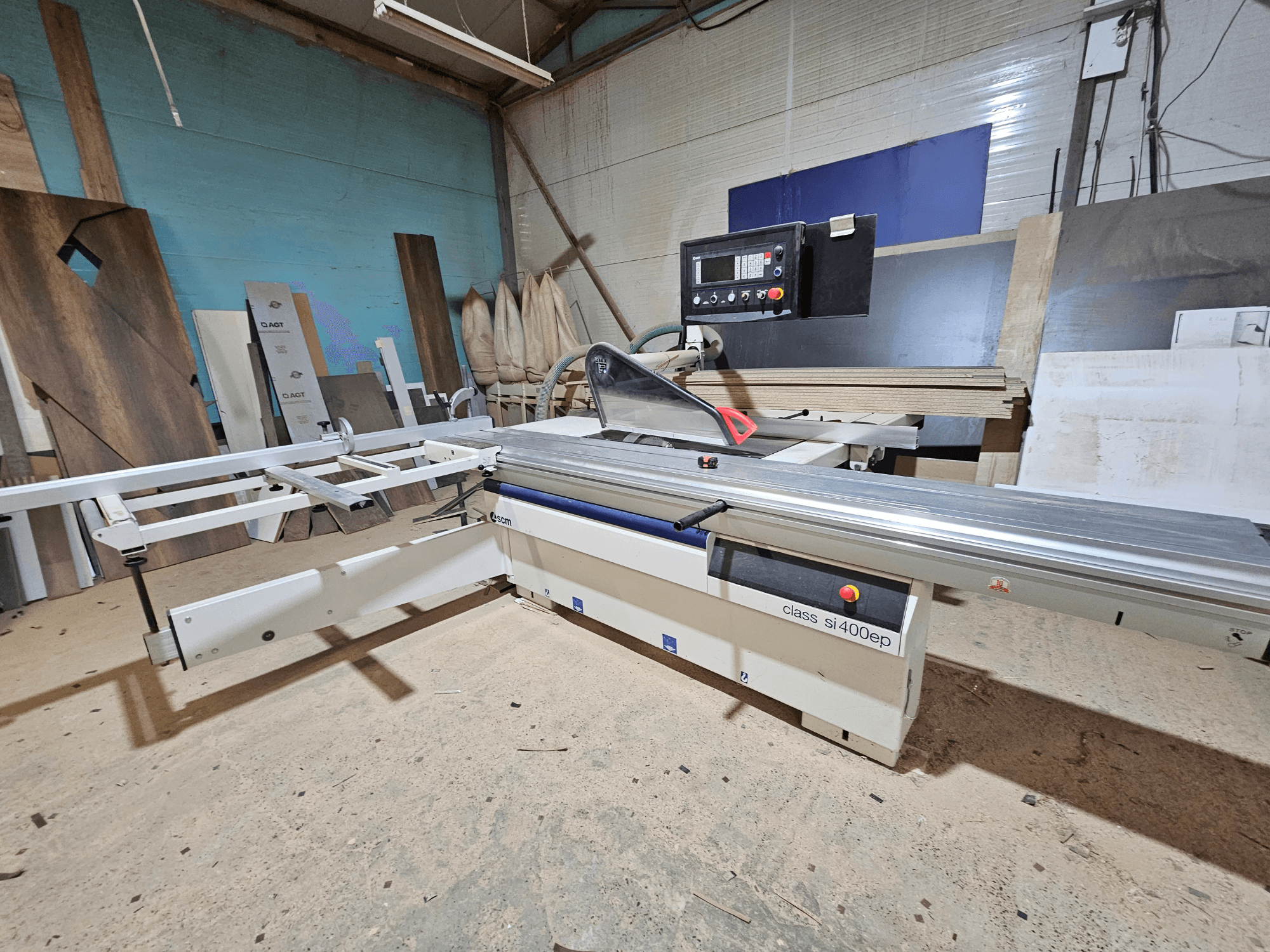 Klassi SI400EP paneelisammas, esiplaanil, reguleeritava tara, asetatud liivapõhjalisele töökojapõrandale, ümbritsetud puitplaatidega.