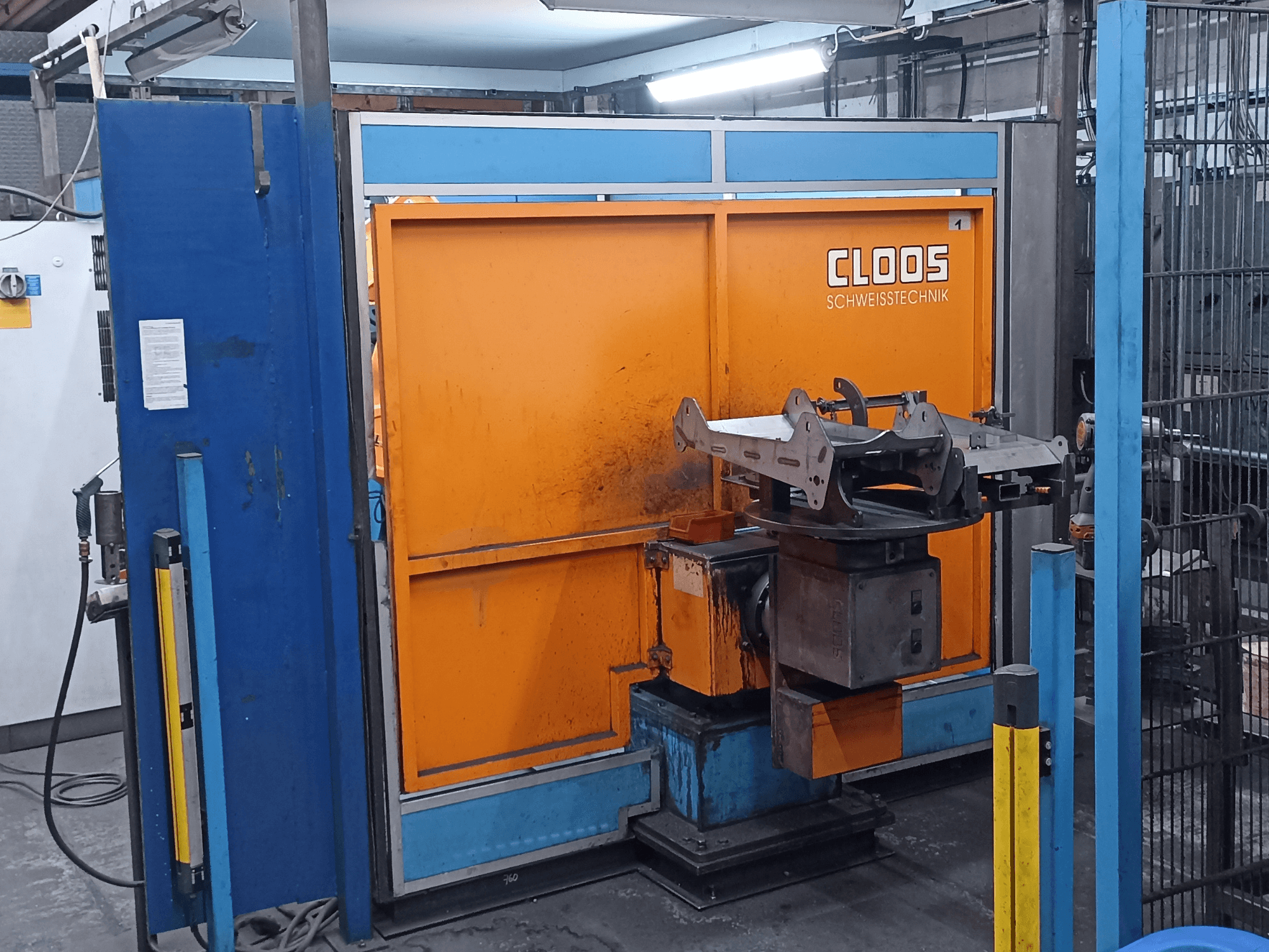 CLOOS Romat 320 keevitusrobot töökodas, vaade eest, oranži juhtpaneeliga ja metallist töödeldava detailiga pöörleval alusel.