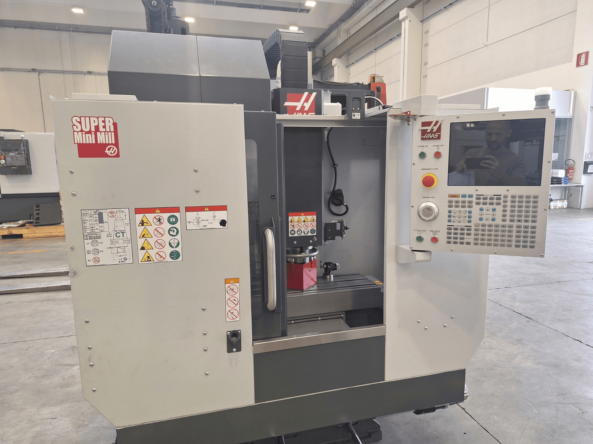 HAAS Super Mini Milli esivaade, millel on näha juhtpaneel, ohutusmärgised ja töötlemisala koos paigaldatud töödeldava detailiga.
