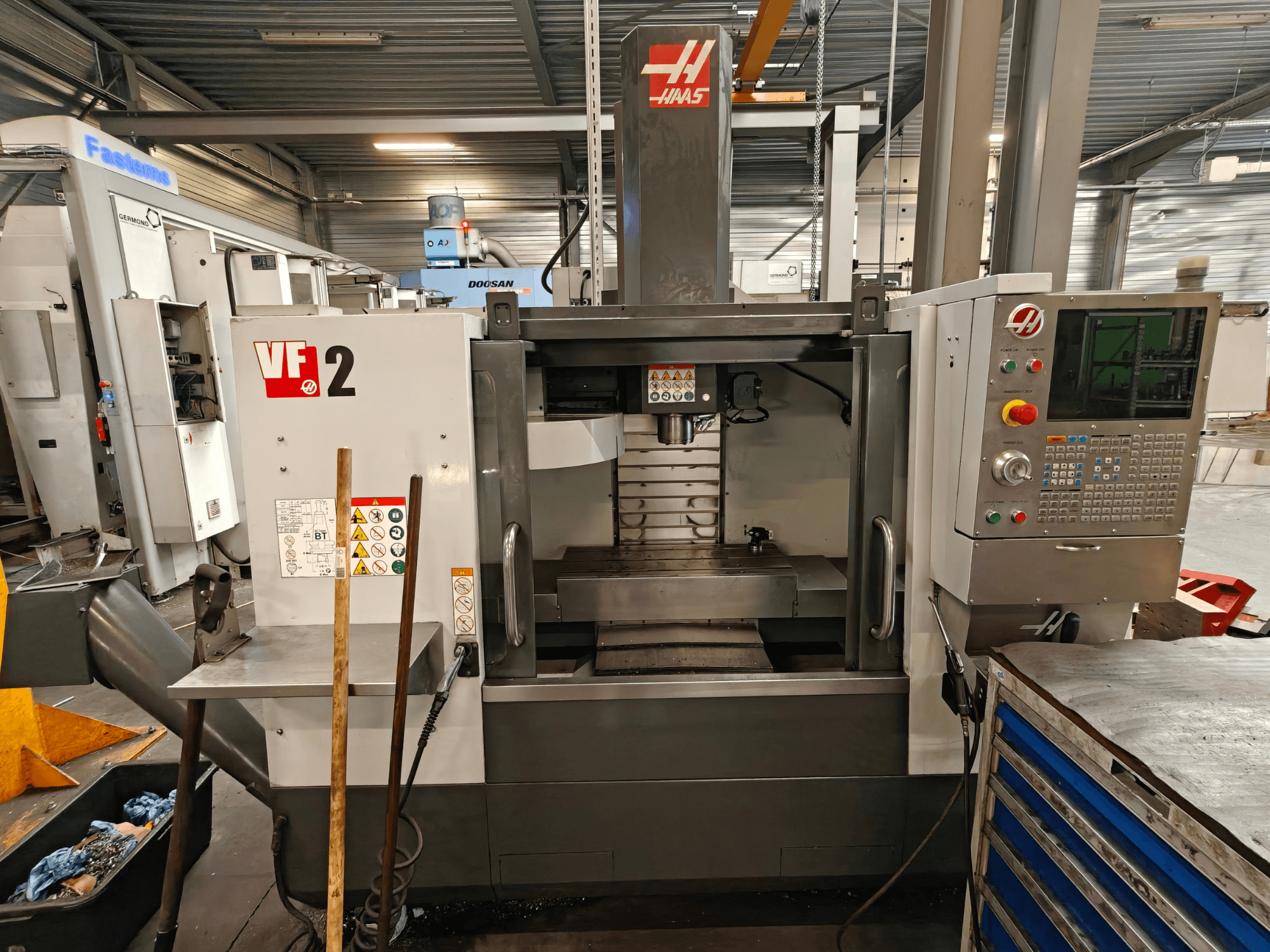 HAAS VF-2 vertikaalne töötlemiskeskus, vaade eest, millel on näha juhtimispaneel, spindel ja tööpink töökoda keskkonnas.