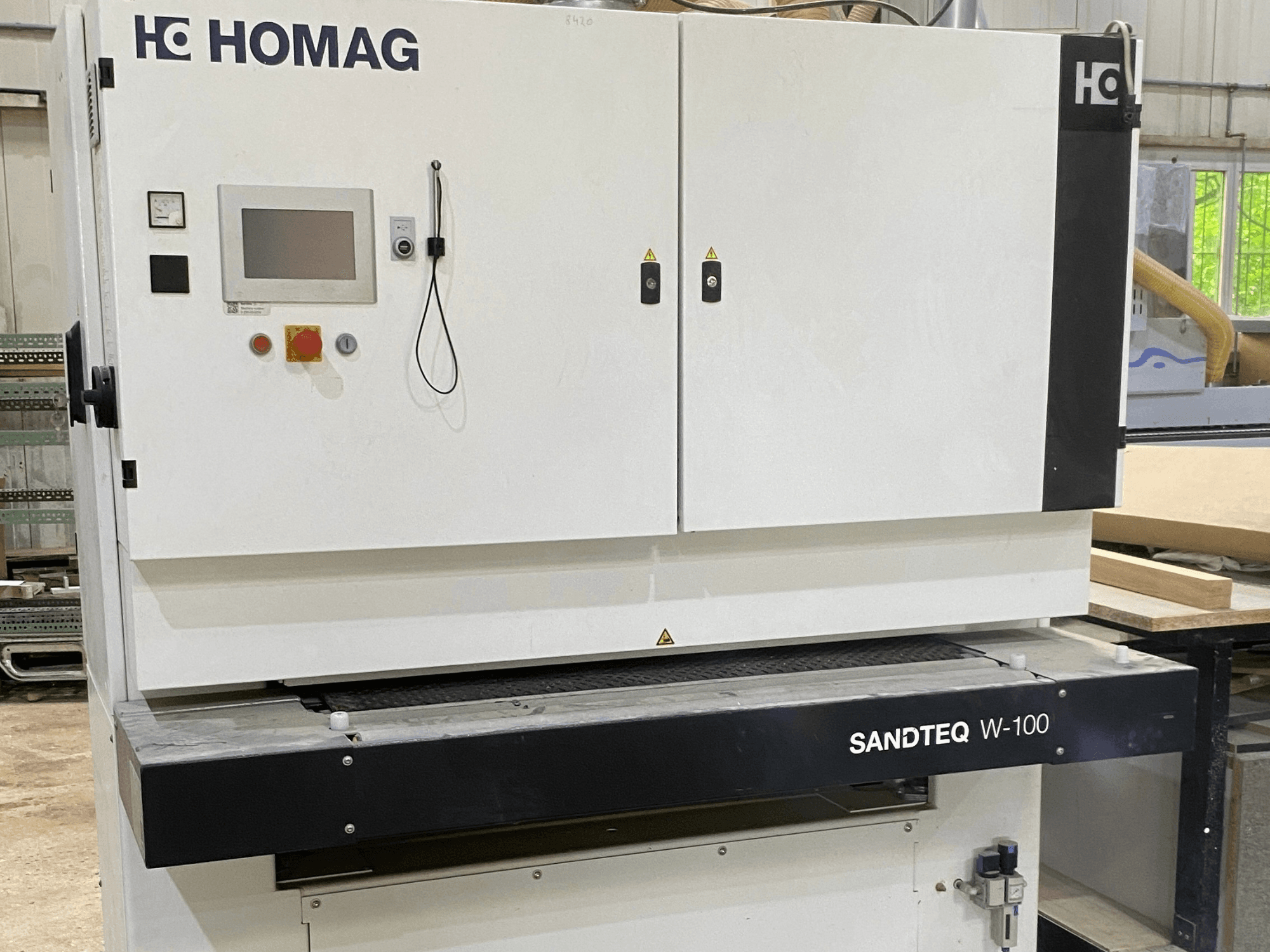 HOMAG SANDTEQ W-100 lintlihvija töökodas, millel on näha juhtpaneel, tolmuäravooluava ja lihvimislinta piirkond. Vaade eestpoolt.
