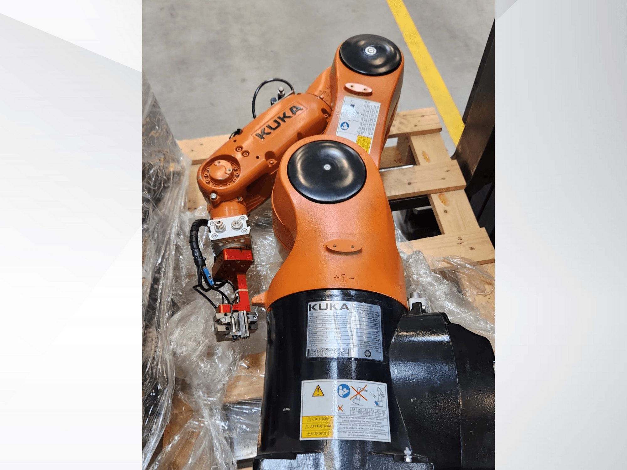 KUKA robotkäsi oranži viimistlusega, külgvaade, millel on haarats ja juhtimisjuhtmestik puidust kaubaalusel.