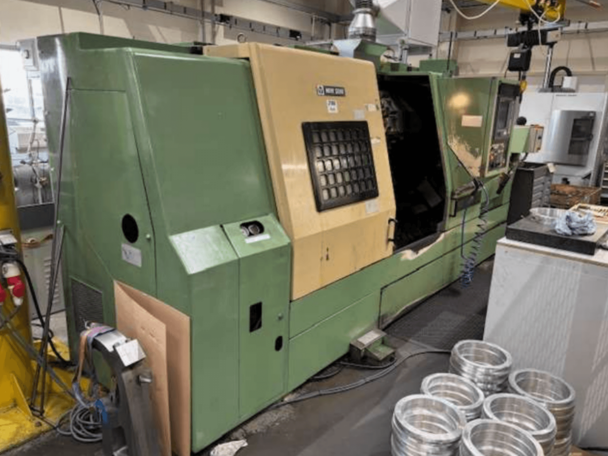 Roheline Mazaki CNC-treipingi masin, mis näitab juhtpaneeli ja töödeldud alumiiniumdetaile töölaual.