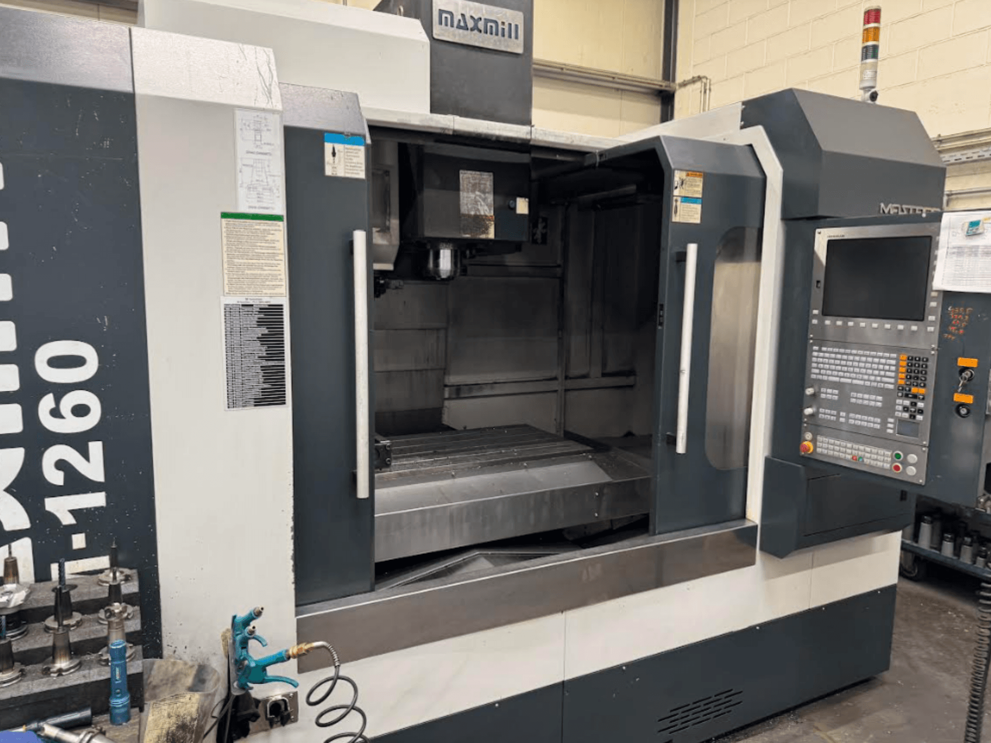 Maxmill CNC-freesping, mudel M-1260, esiplaanil tühi tööruum koos juhtpaneeli ja kasutusjuhendiga.