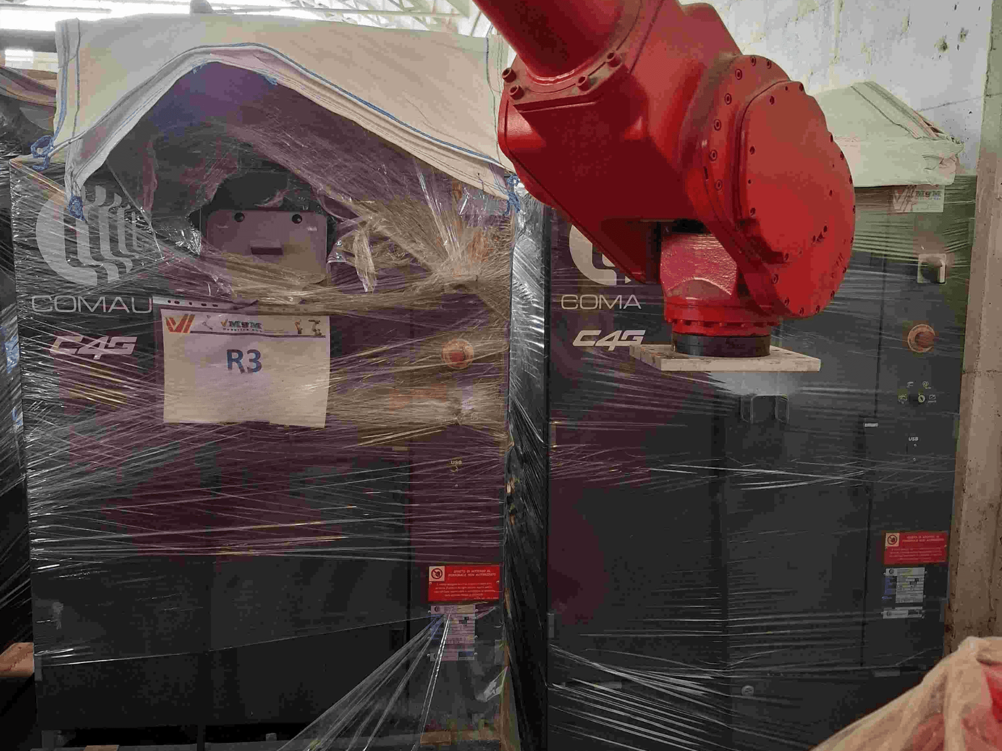 Comau C4G robotkäsi esiplaanil, plastmassiga ümbritsetud, märgistatud "R3", masina peal on näha hoiatuskleebised.