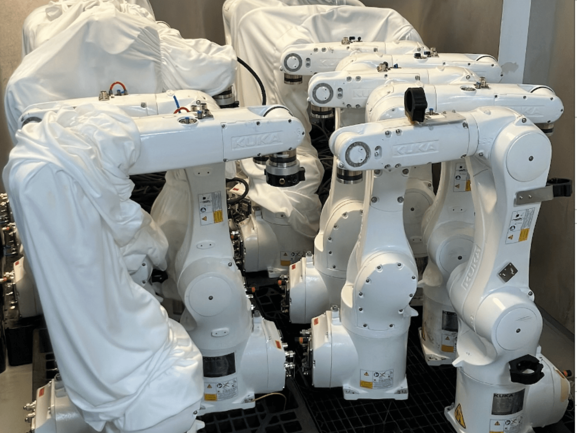 KUKA KR 10 R900-2 robotkäsi, kaetud valge kangaga, ülaltvaates, kus on näha mitu seadet laos.