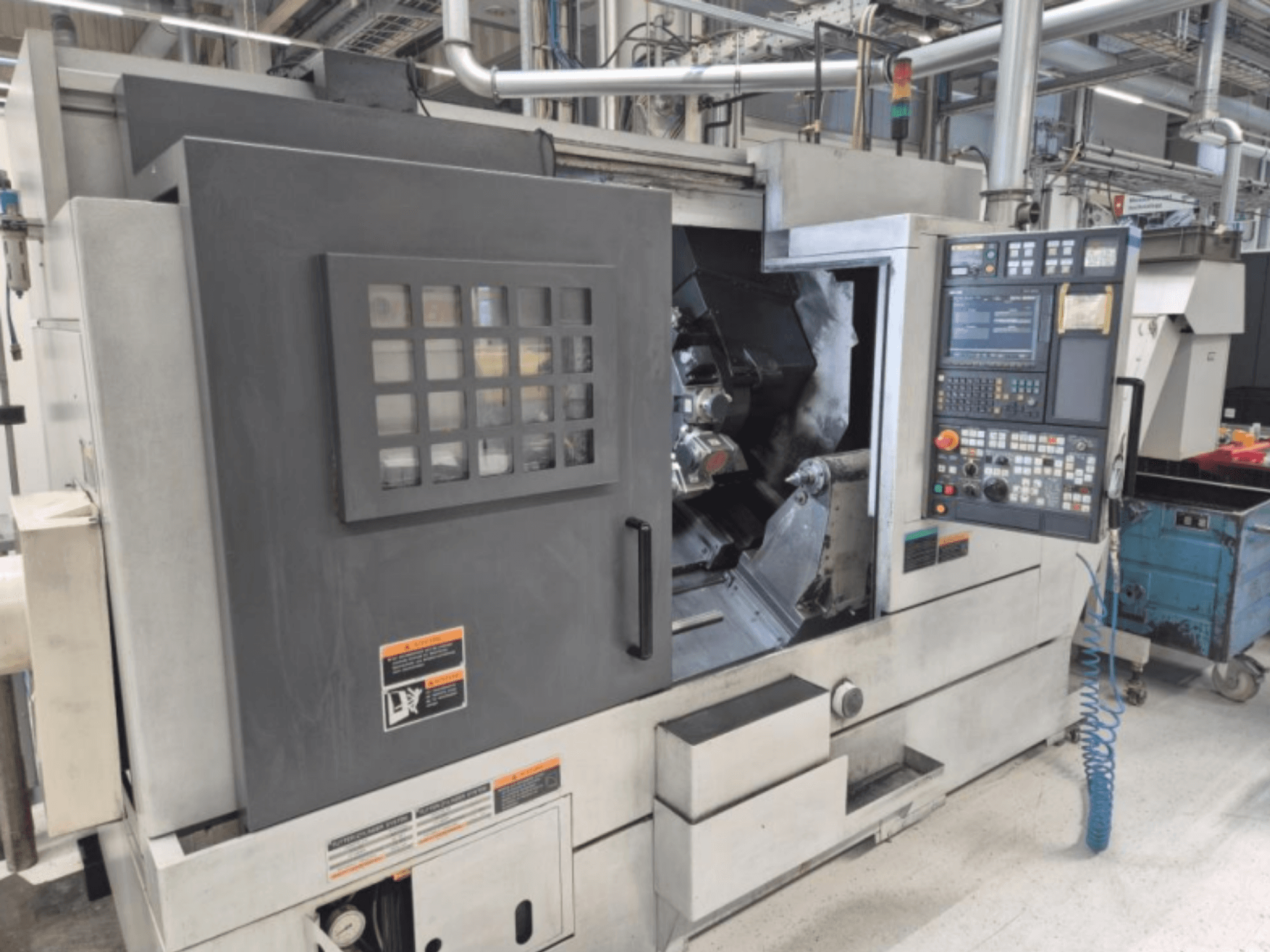 CNC-tööpinklaas koos juhtpaneeliga, esiplaanil. Omab nähtavat tööala ja turvaakent, kaubamärk teadmata.