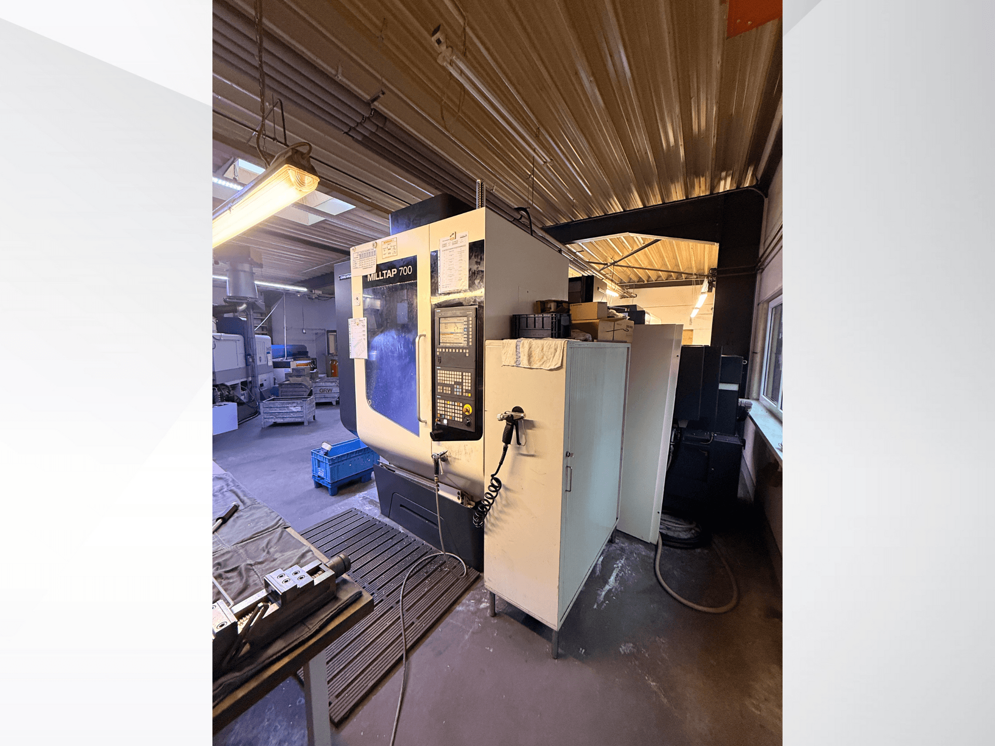 Milltap 700 CNC-tööpink töökojas; esiplaanil on juhtpaneel, tööriistariiulid ja ladustamisalad, mille kohal on valgustus.