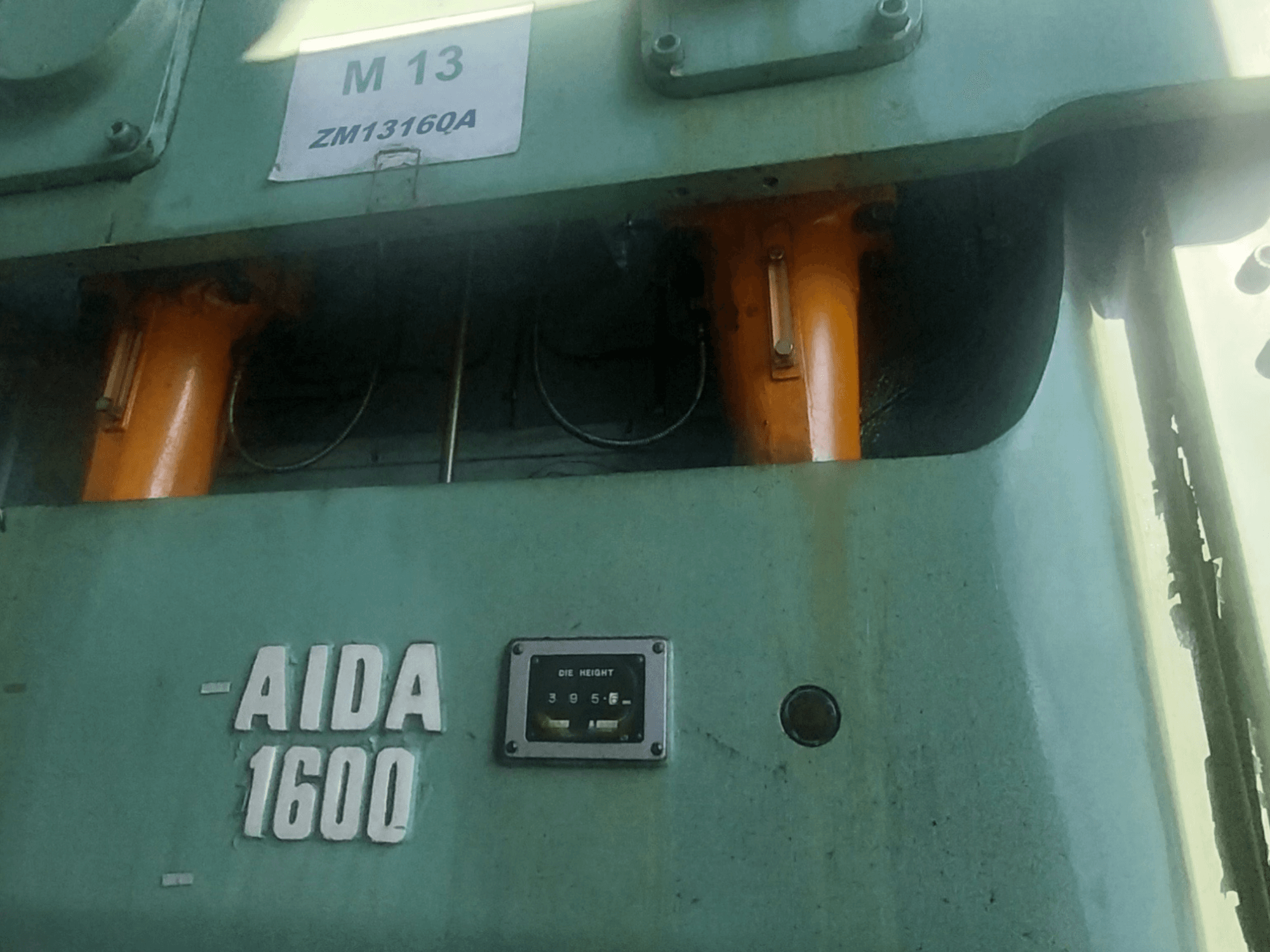 AIDA NC2-1600 mehaaniline stantsimispress, esiplaanil; näha oranžid hüdraulikakomponendid ja stantsi kõrguse mõõtur.