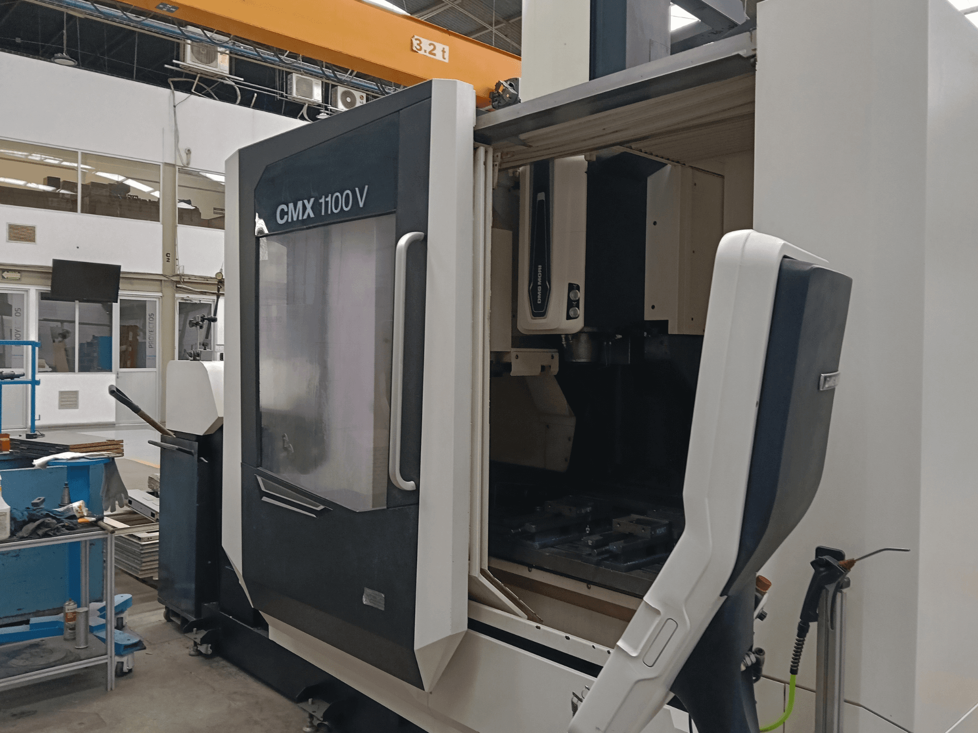 DMG MORI CMX 1100 V vertikaalne töötlemiskeskus, esivaade, millel on näha avatud uks ja seadme sisemine tööriistade paigutus tööstusruumis.