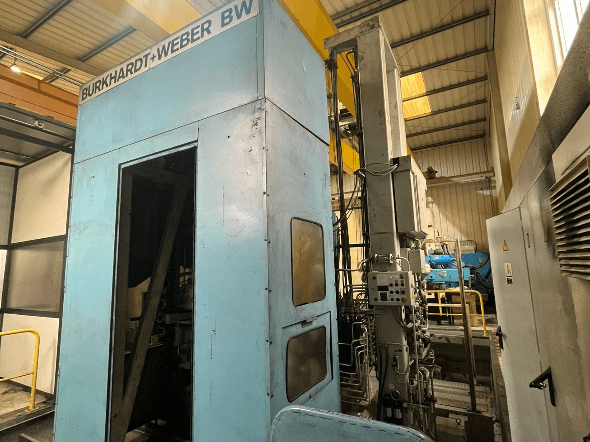 Burkhardt-Weber MC100 horisontaalne töötlemiskeskus, külgvaade, millel on näha sinine väliskorpus ja juhtpaneel koos nähtavate torudega.