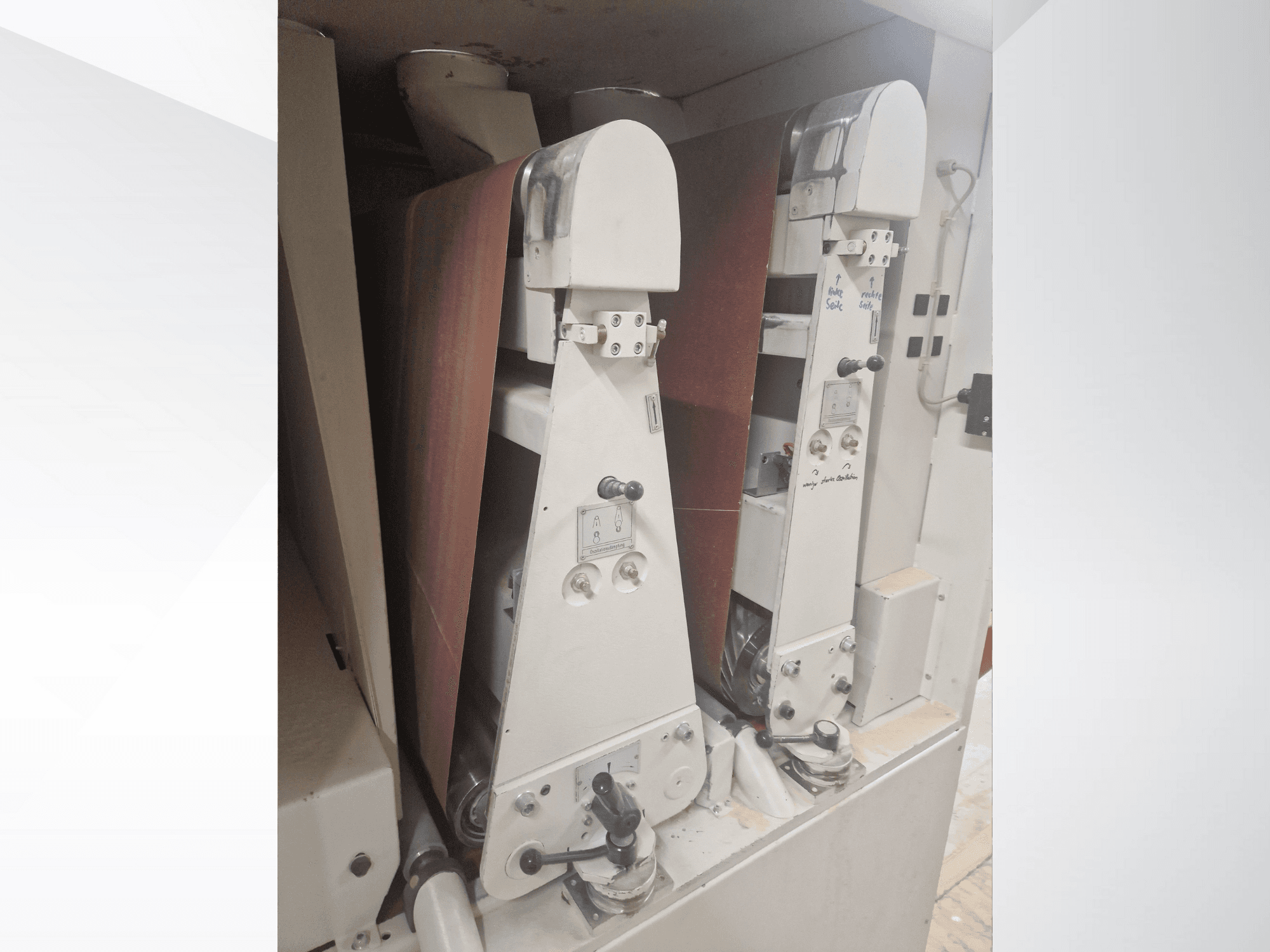 Kaks tööstuslikku lihvimismasinat punaste lihvimisrihmadega, esivaade, kus on näha juhtimisseadmed ja metallosad.