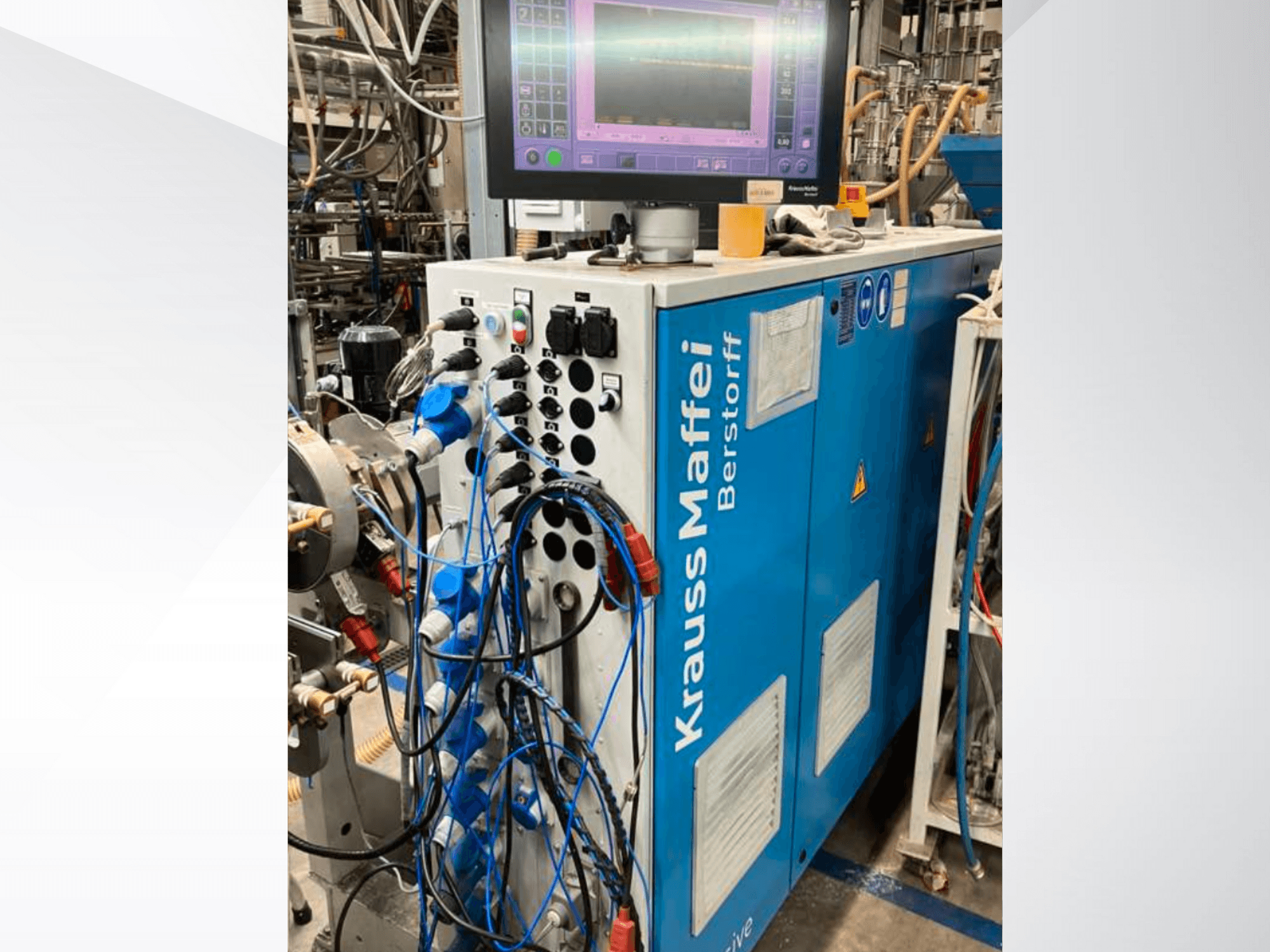 Krauss Maffei Berstorffi tööstuslik masin koos juhtpaneeli ja monitoriga, millel on erinevad nupud ja ühendatud voolikud, külgvaade.