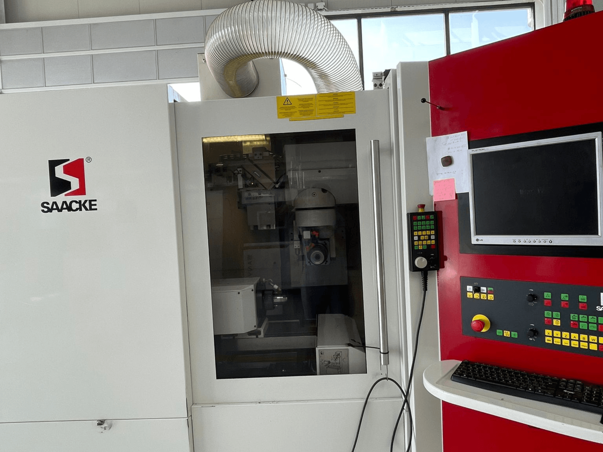 Valge ja punane SAACKE masin, esiplaanil, millel on juhtpaneel, monitor ja nähtavad sisemised osad läbi klaasi.