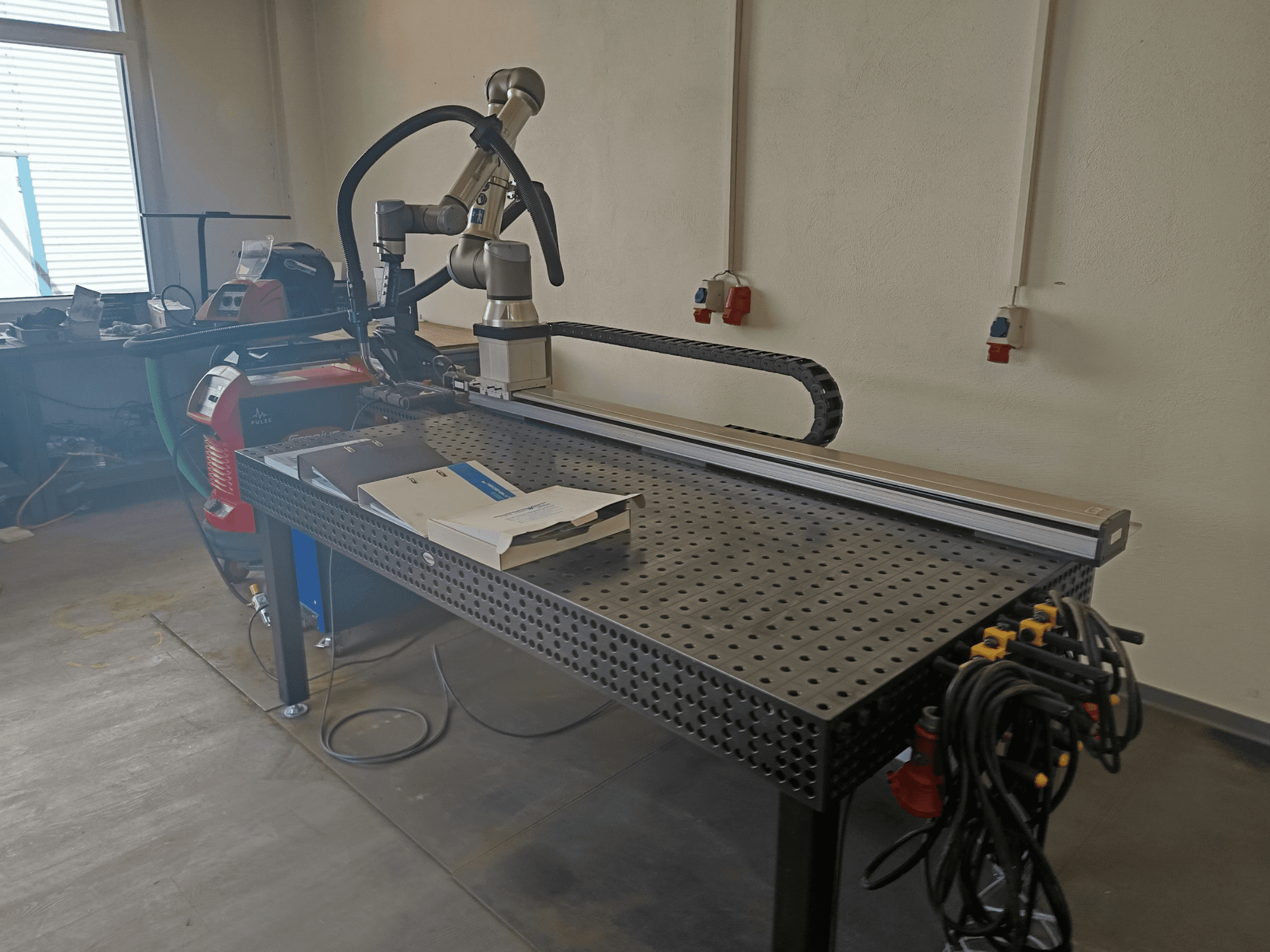 FRONIUS TransSteel 4000 impulsskeevitusseade külgvaates, millel on robotkäsi, tööala ja toiteühendused.