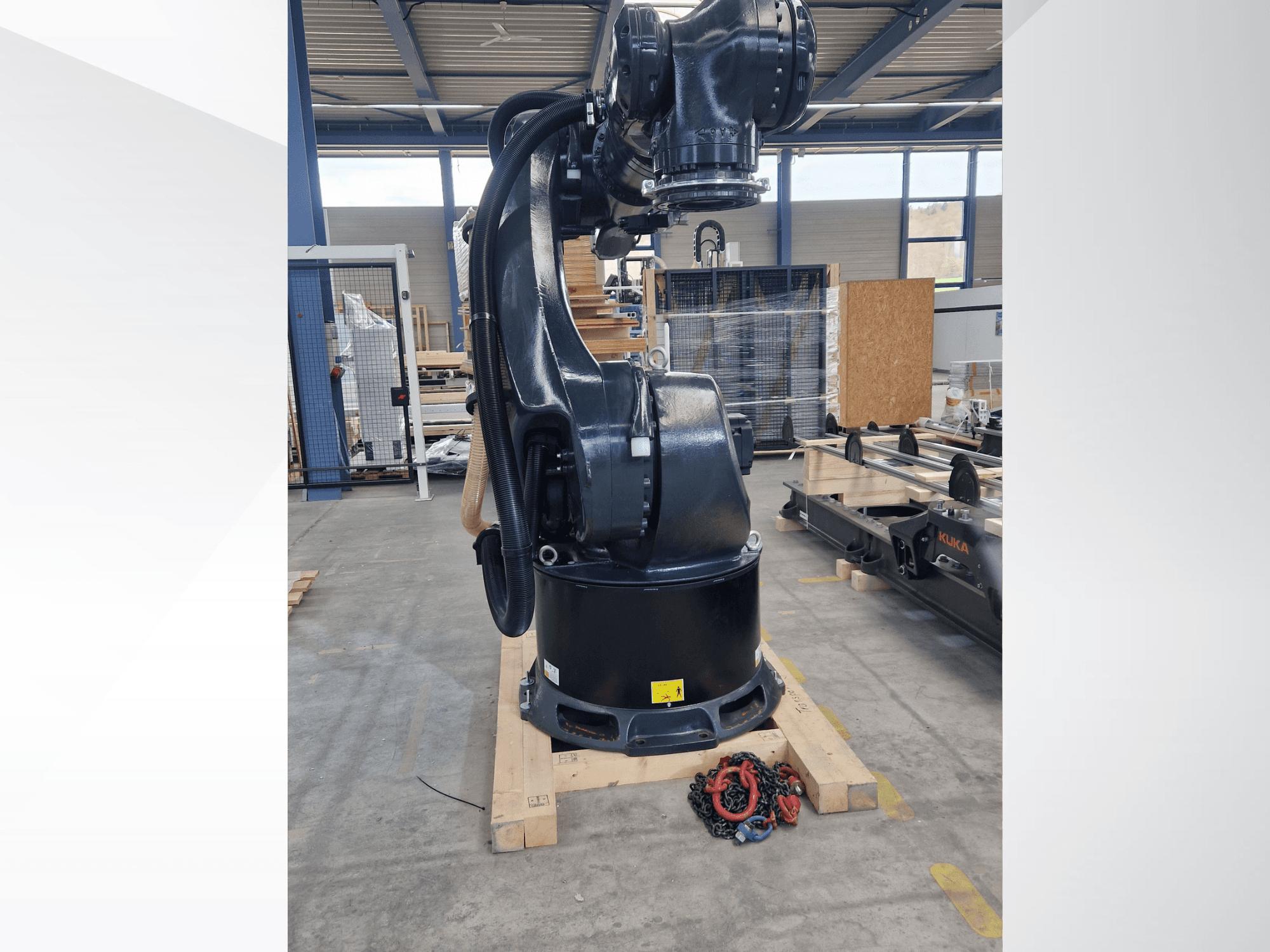 KUKA KR 340 R3330 robotkäsi laos, külgvaade, millel on näha alus ja kaablid, esiplaanil ketid.